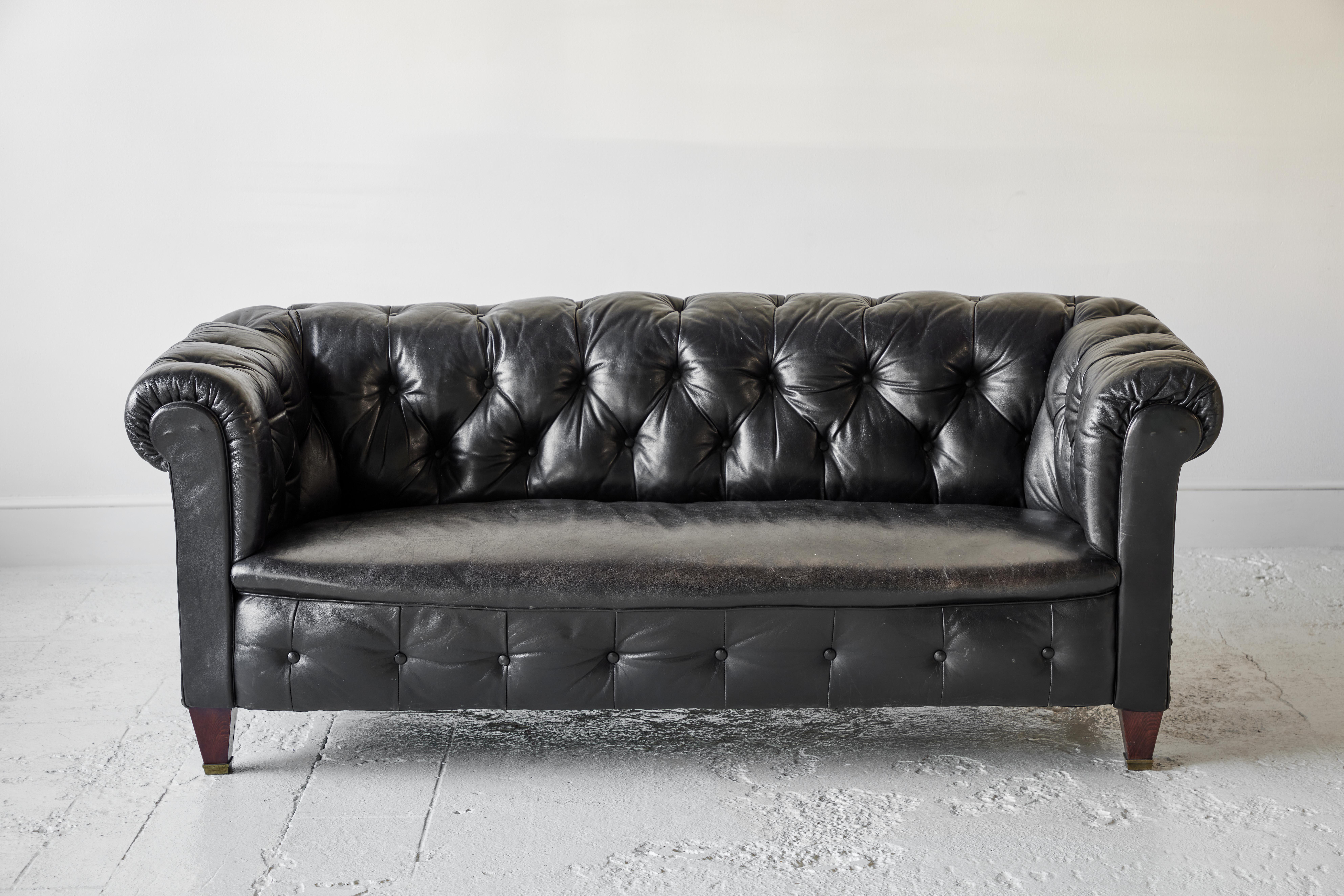 Black leather tufted chesterfield sofa with single seat cushion.