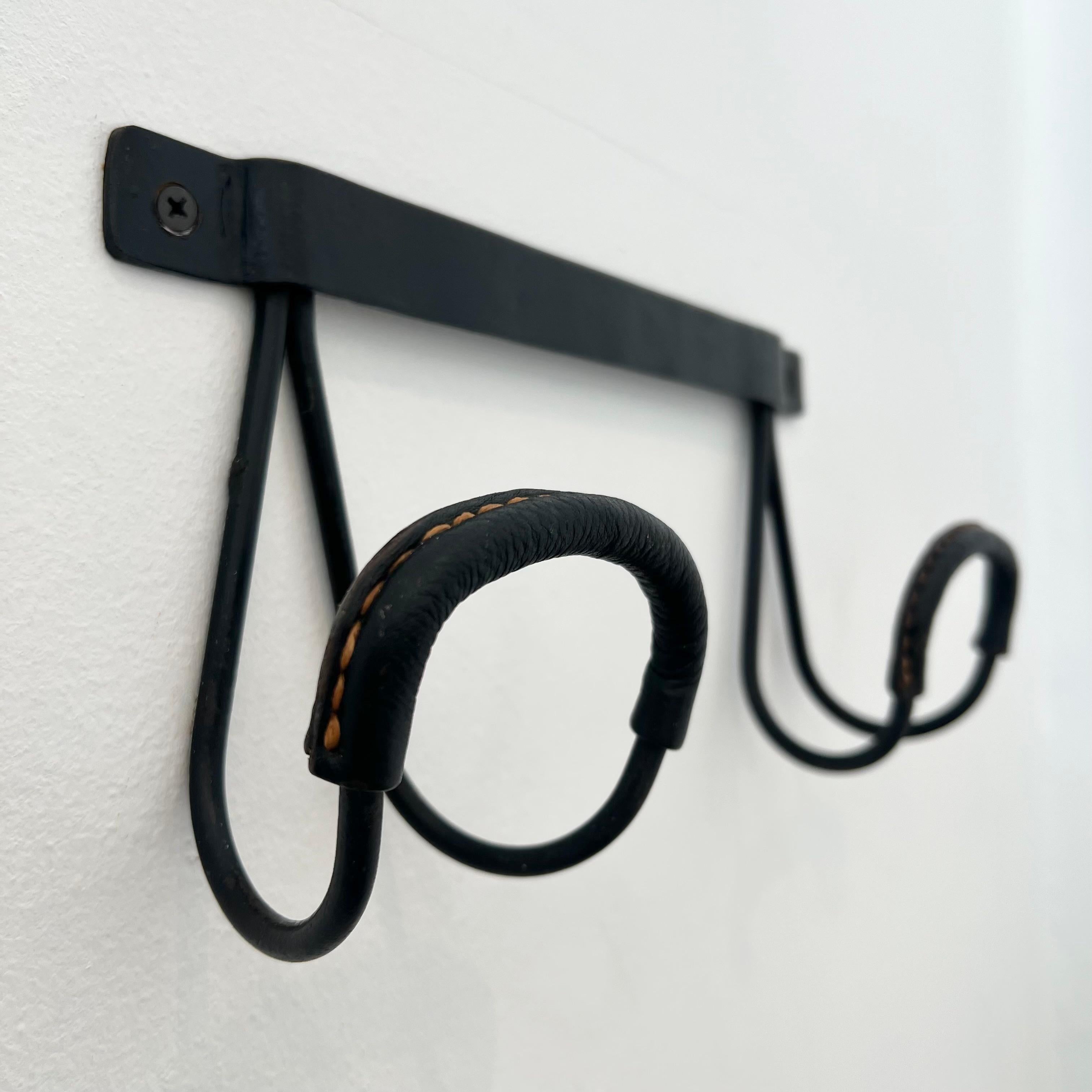 Un appendiabiti classico del designer francese Jacques Adnet. I ganci in ferro nero sono  in pelle nera, con le cuciture a contrasto tipiche di Adnet. Buone condizioni vintage con poca usura. Come ogni altro pezzo di Adnet, questo appendiabiti è