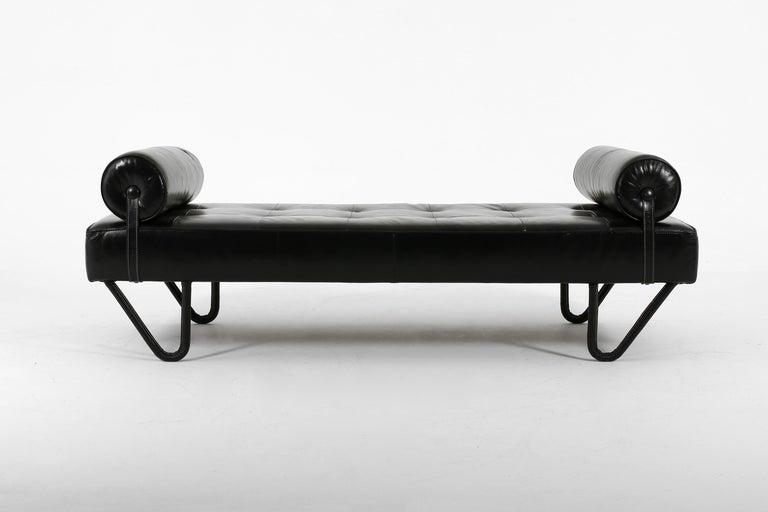 A black leather clad daybed with two bolster cushions by Jacques Adnet. Featuring contrast saddle stitching to the hairpin legs and bolster straps, which attach to the base by way of a metal press stud. French, c. 1950s.