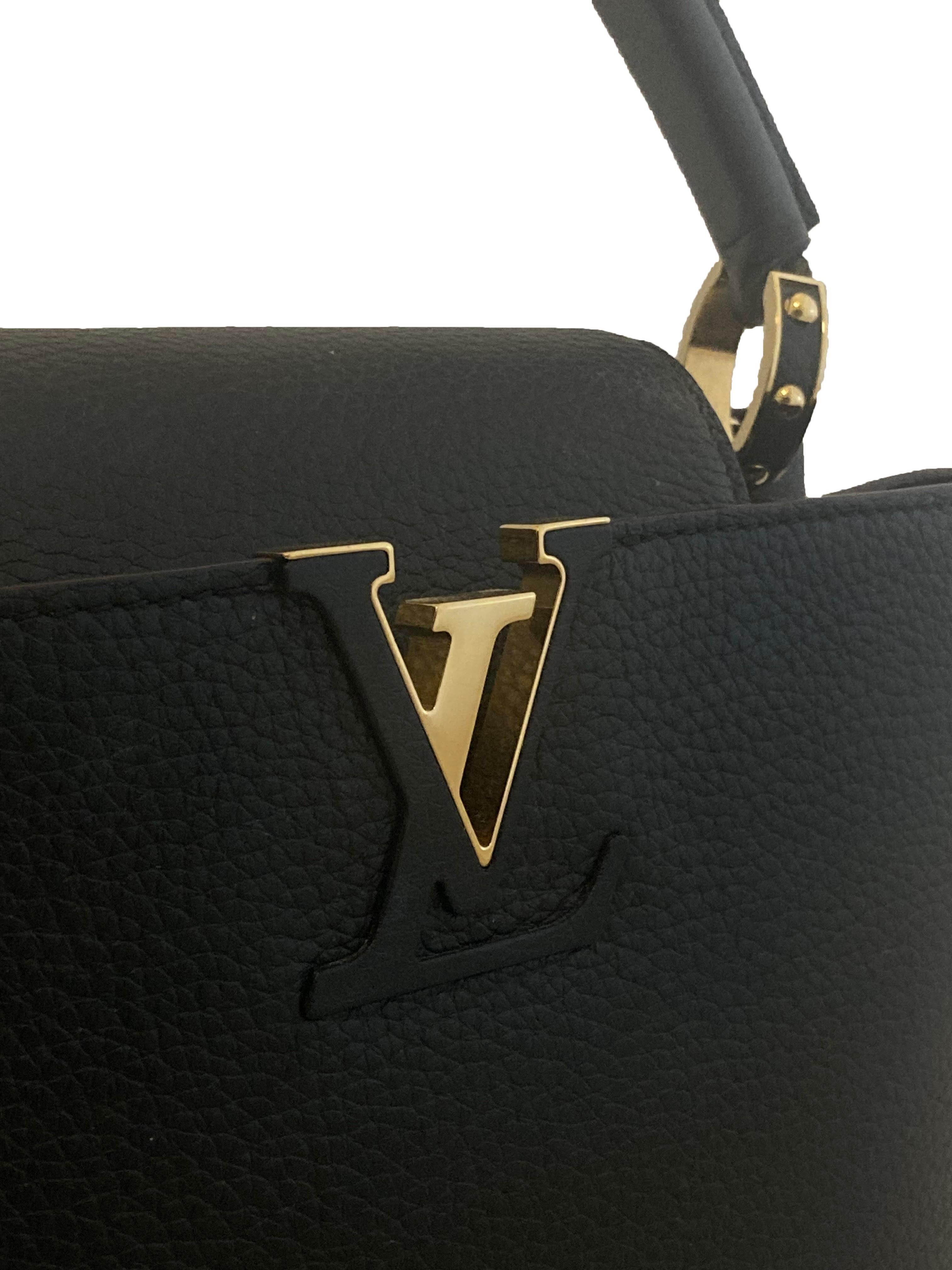 Black leather Capucine BB handbag from Louis Vuitton. Black textured Taurillon leather upper with shiny gold toned hardware. Branded with an interlocking 'LV' on the front in leather and gold. Single rolled leather top handle is fastened metal and