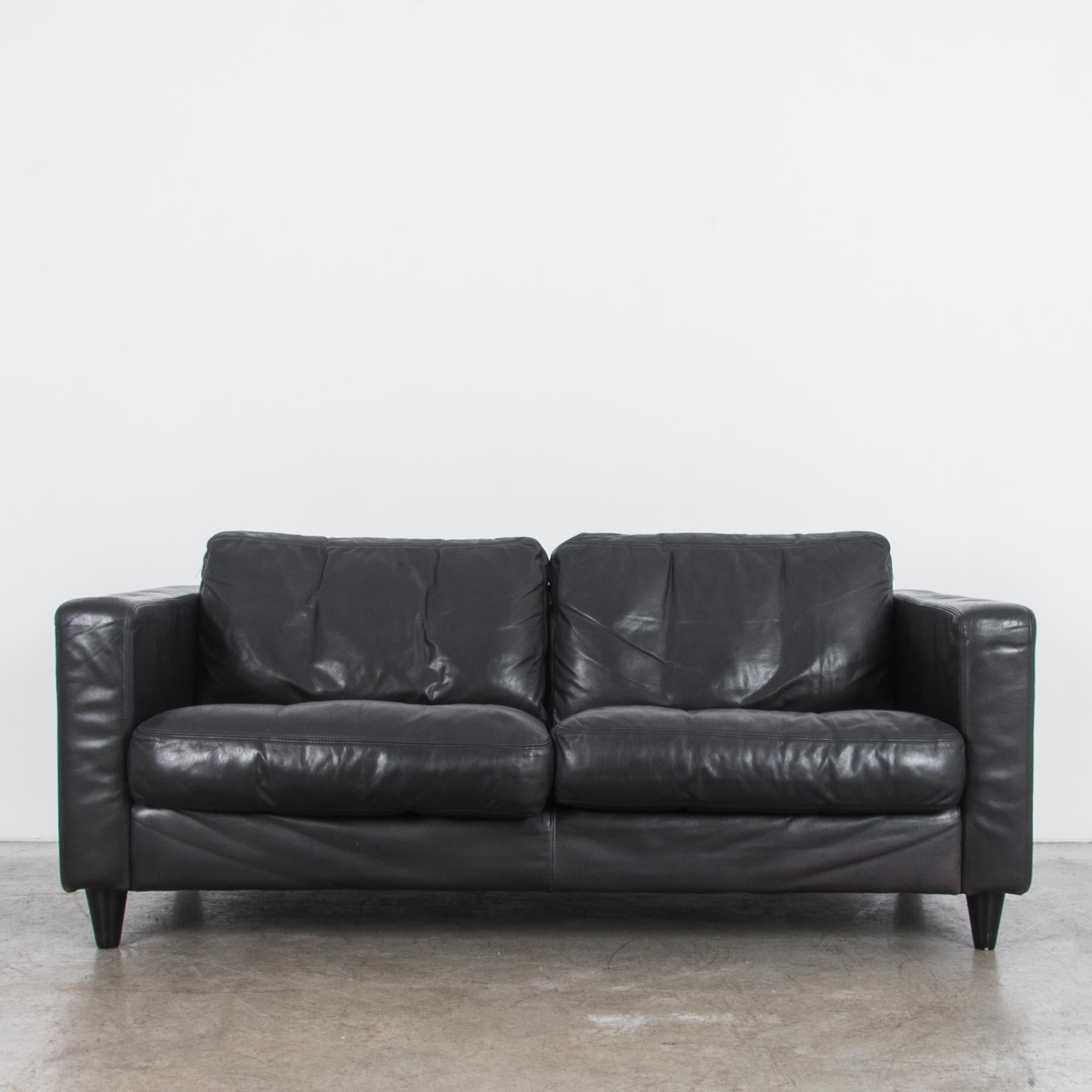 A black leather sofa by German furniture design studio Machalke, circa 1970. The wide cubic frame of the “Pablo” design speaks to a modern sensibility, while raised sofa legs give this piece a comfortable shape. The detailed leather workmanship is a