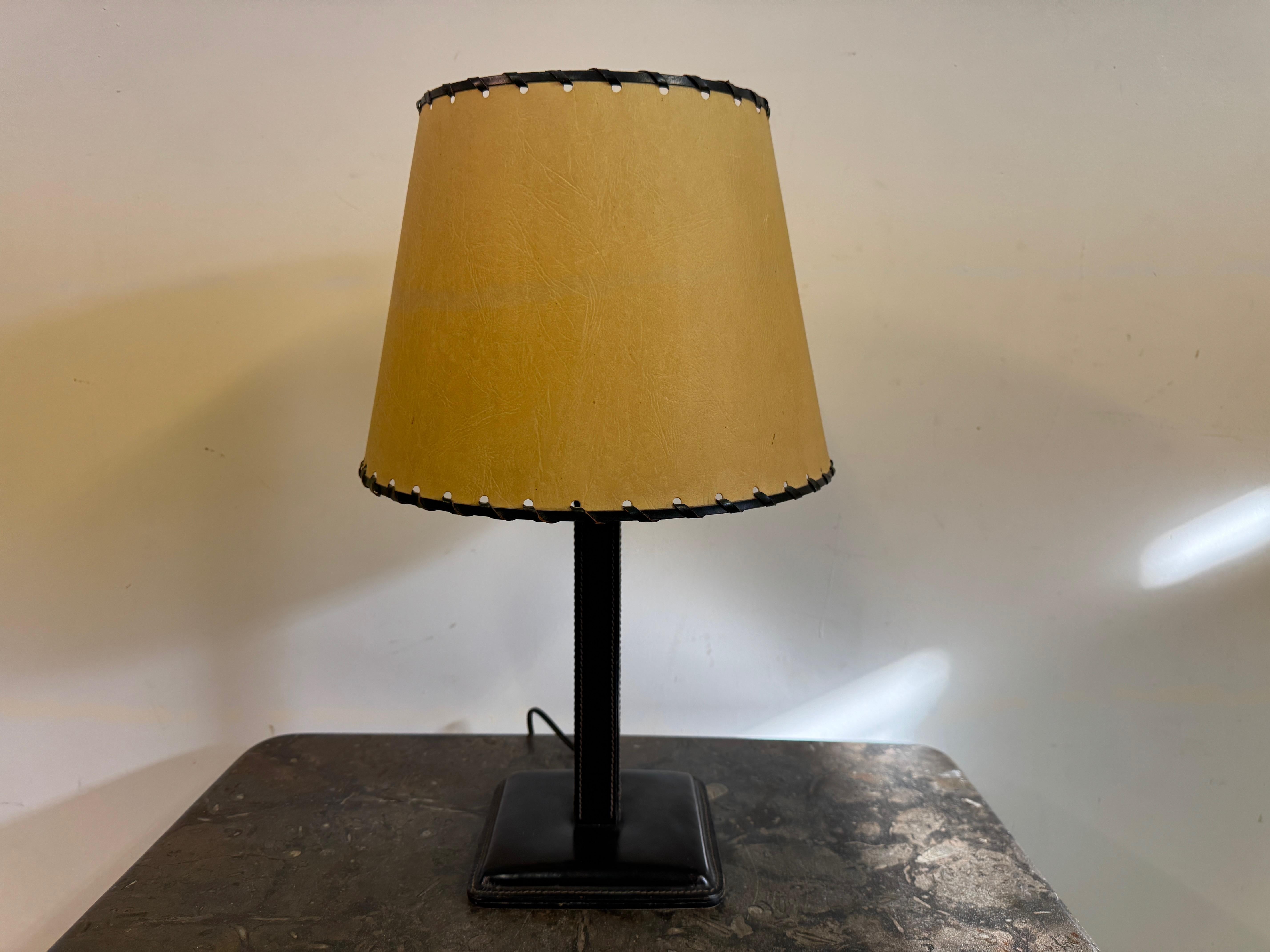 Lampada da tavolo rivestita in pelle

Una sofisticata lampada da tavolo nello stile di Jacques Adnet, che incarna l'eleganza senza tempo del design francese di metà secolo. La lampada è dotata di una base e di uno stelo rivestiti in pelle nera,