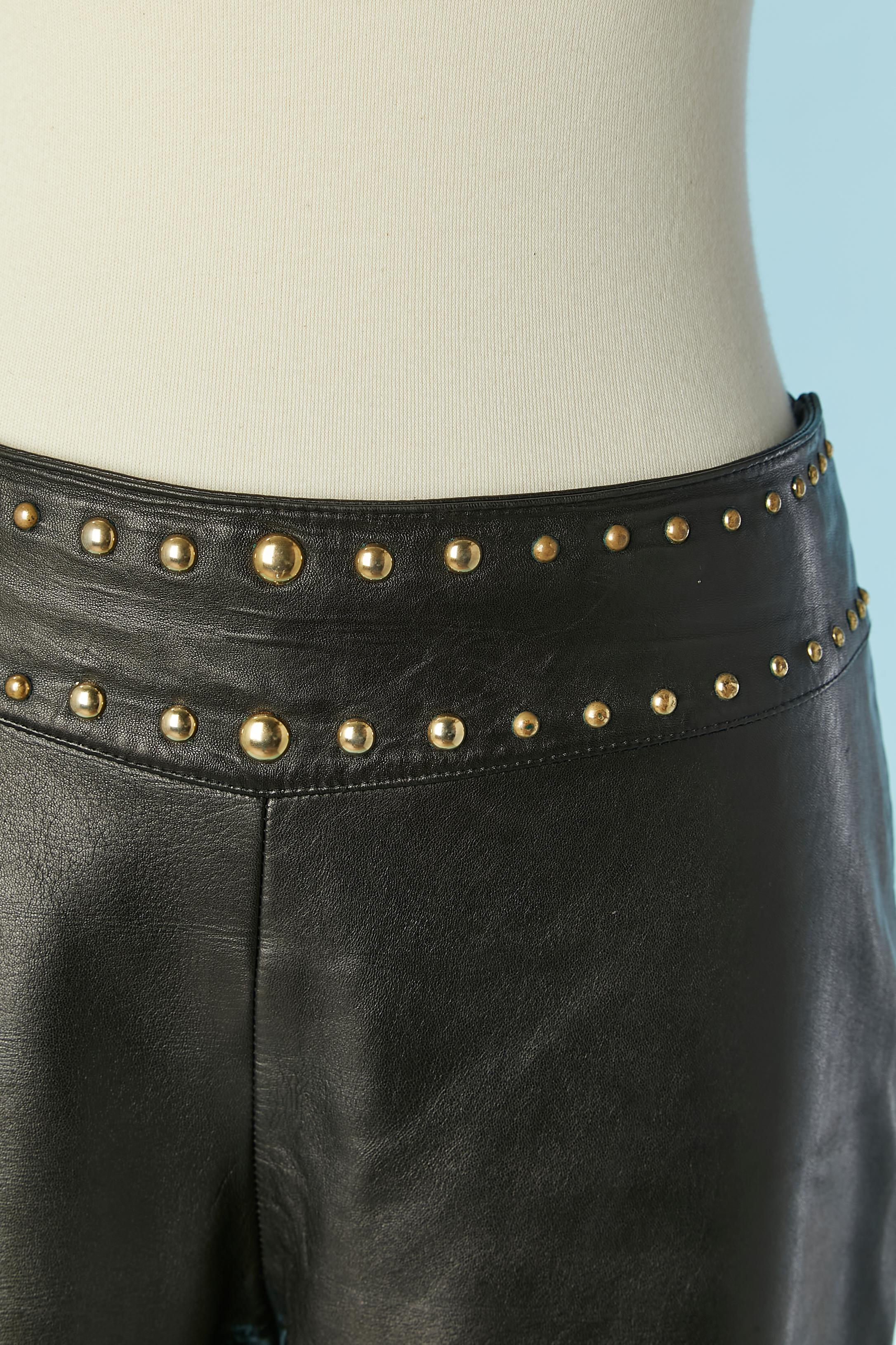 Pantalón de cuero negro con tachuelas de metal dorado en la cintura. No hay etiqueta de composición del tejido, pero probablemente el forro sea de rayón. 
Cierre con cremallera y corchete en el lado izquierdo. Trabajo de corte en las rodillas.