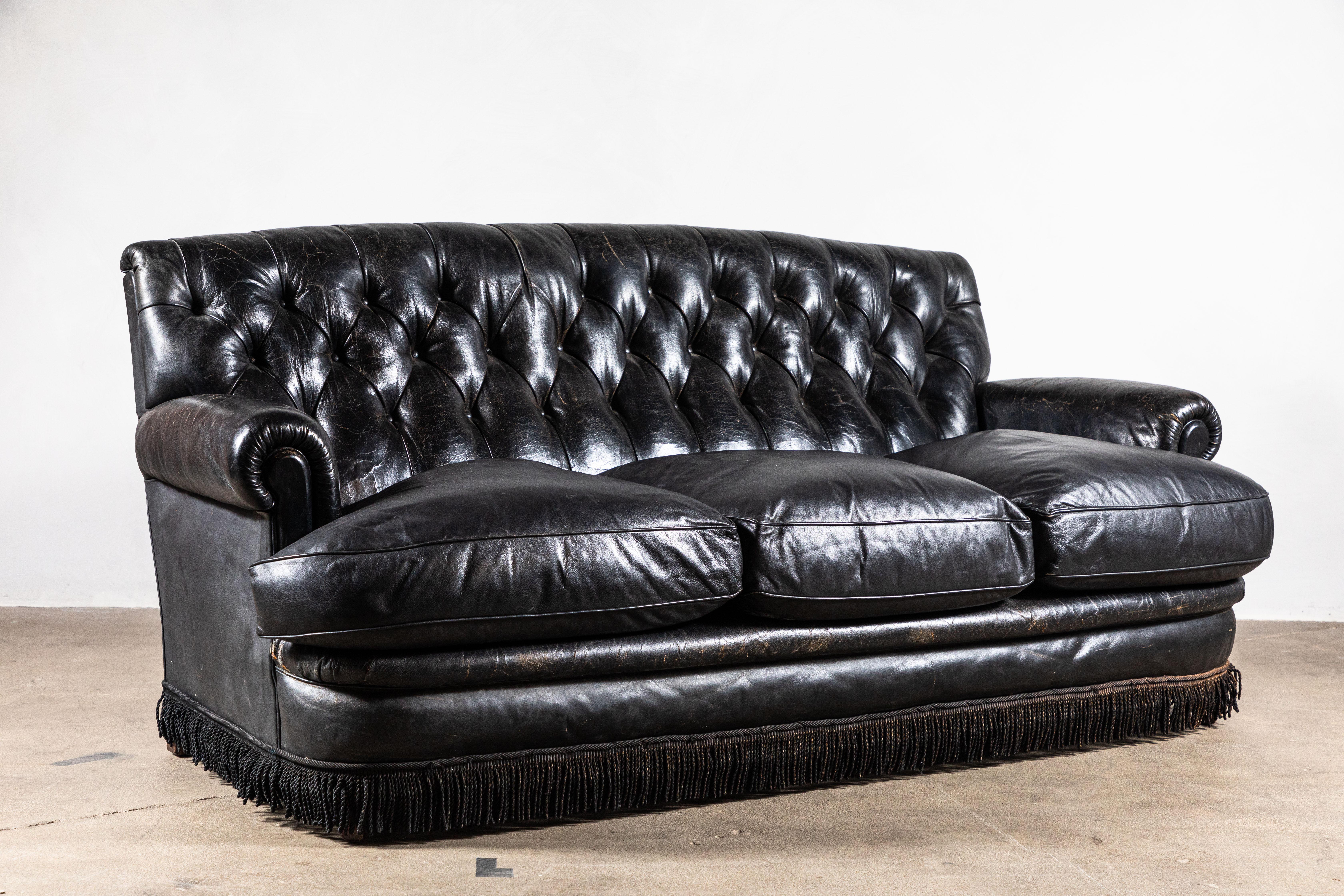 Black leather tufted sofa with three loose seat cushions. The sofa is finished with original fringe details.