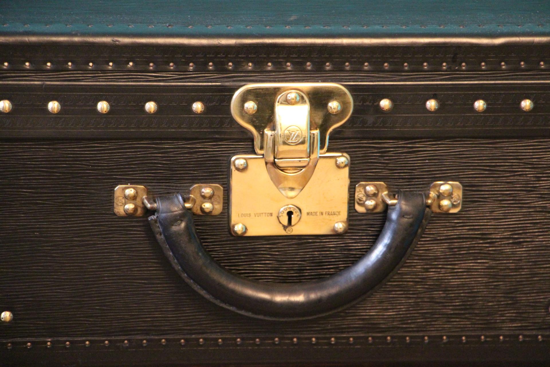 This top of the range all black leather Alzer 70 rigid suitcase features black leather trim, all solid brass LV stamped lock, clasps and studs. Large leather handle.
Its interior is in excellent condition, as new. It is lined in grey suede, with