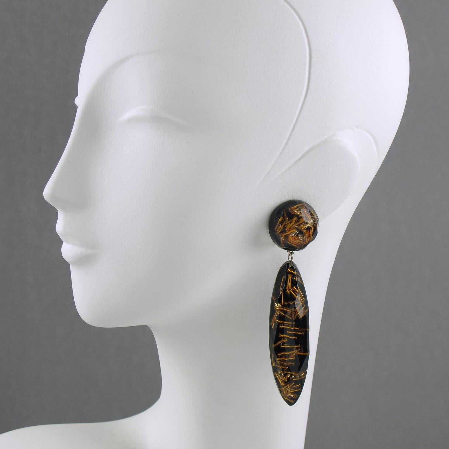 Lovely French oversized Lucite clip-on earrings. Featuring dangling shape, with an extra-long drop carved and faceted bead, compliment with gilt stick beads inclusions over black background. No visible maker's mark.
Measurements: 3.94 in. long (10