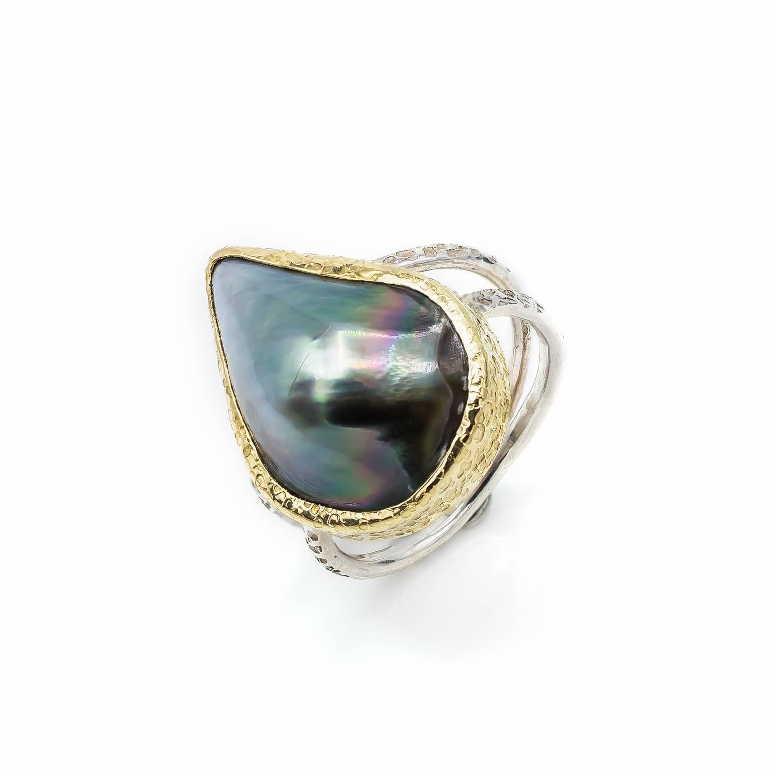 This stunning large black mabe pearl ring is naturally formed in a tear drop fashion from the black lipped oyster. With a slight gradient from the tip to the base this pearl glows in a brilliant silver color with a textured, hammered, 14K yellow