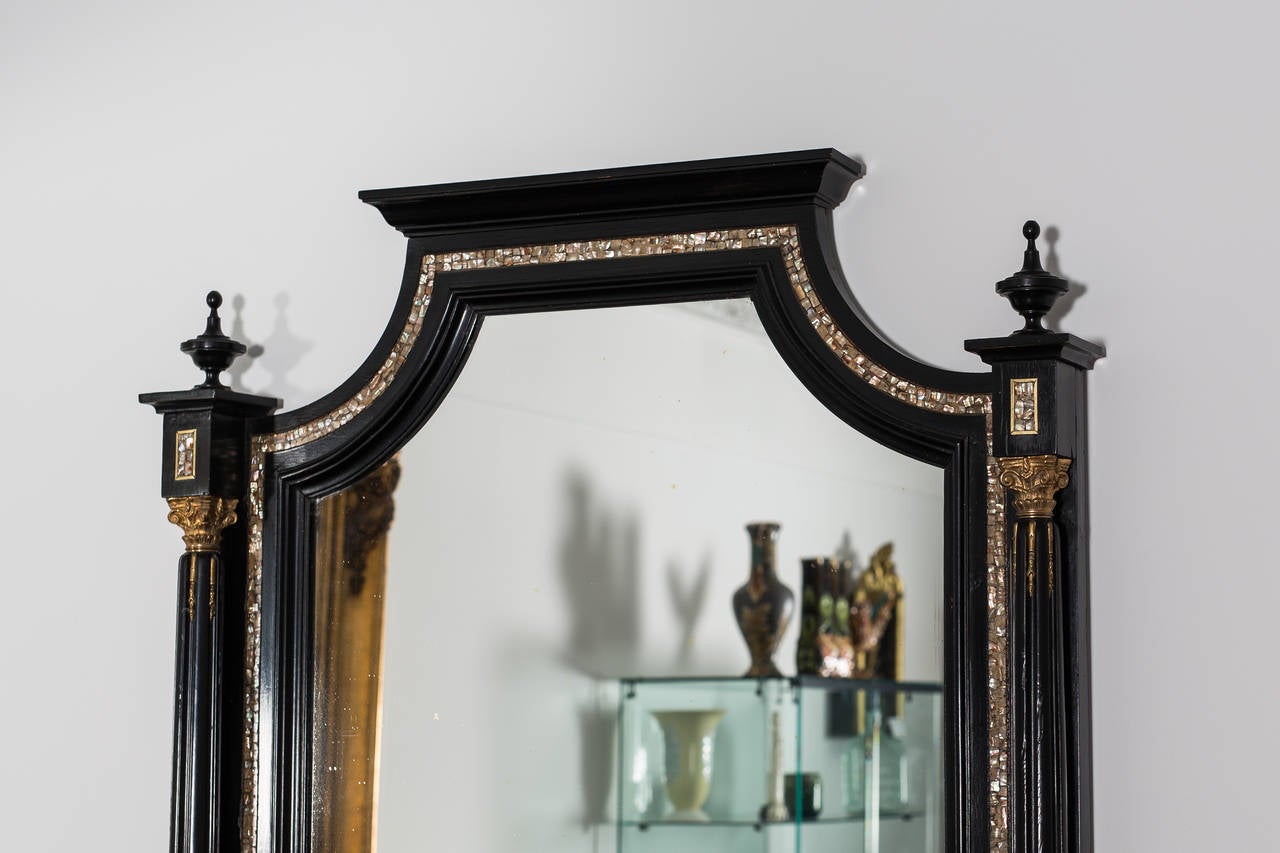 Massive black makart mirror from circa 1880 in Austria. The fantastic carved frame impresses with a very unique shape and was made from solid fruitwood that has been ebonized. Intricate brass stripes and lovely mother of pearl inlays surround this