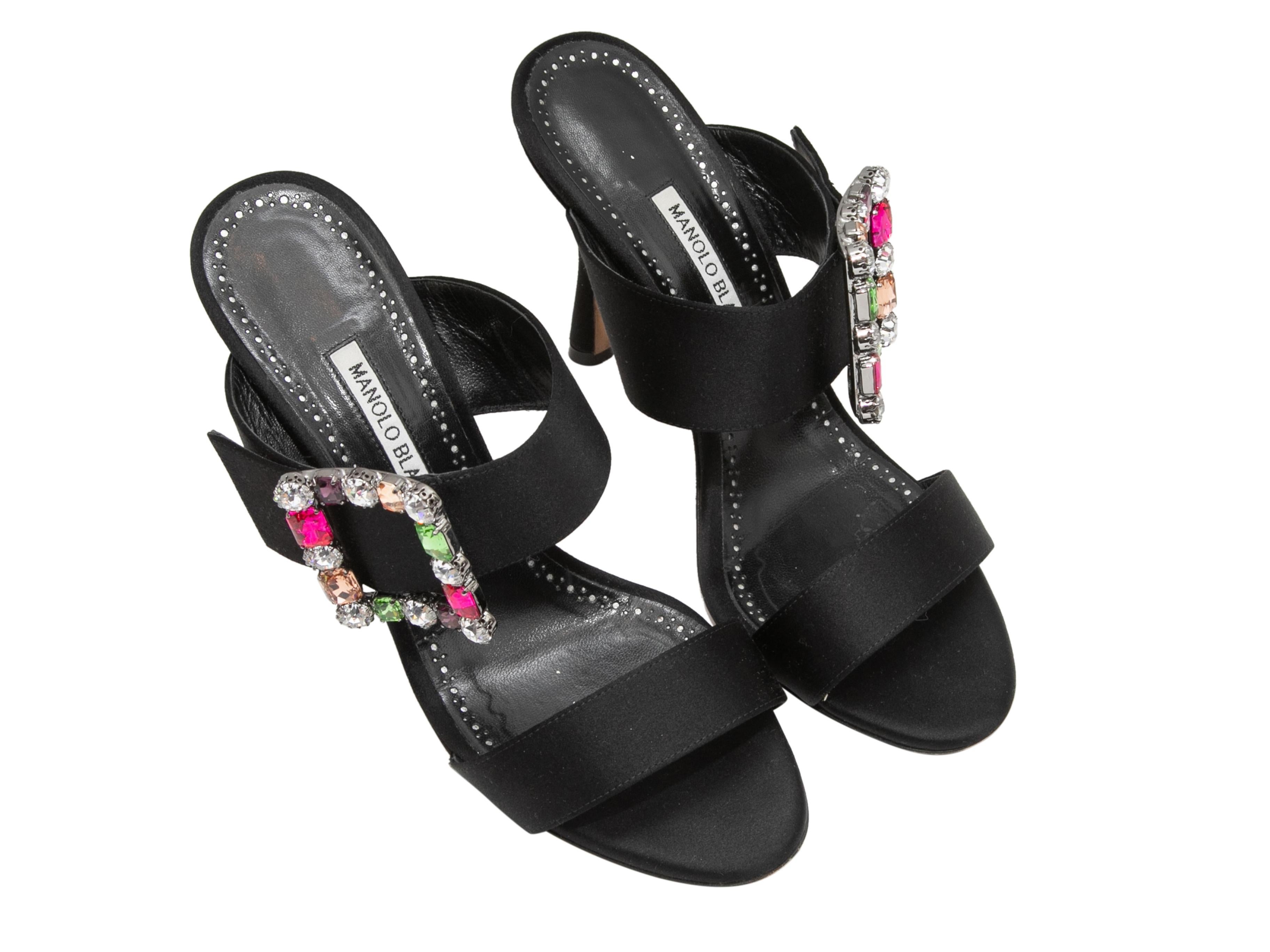 Black satin heeled sandals by Manolo Blahnik. Gemstone-embellished buckle adornments at tops. 4.25