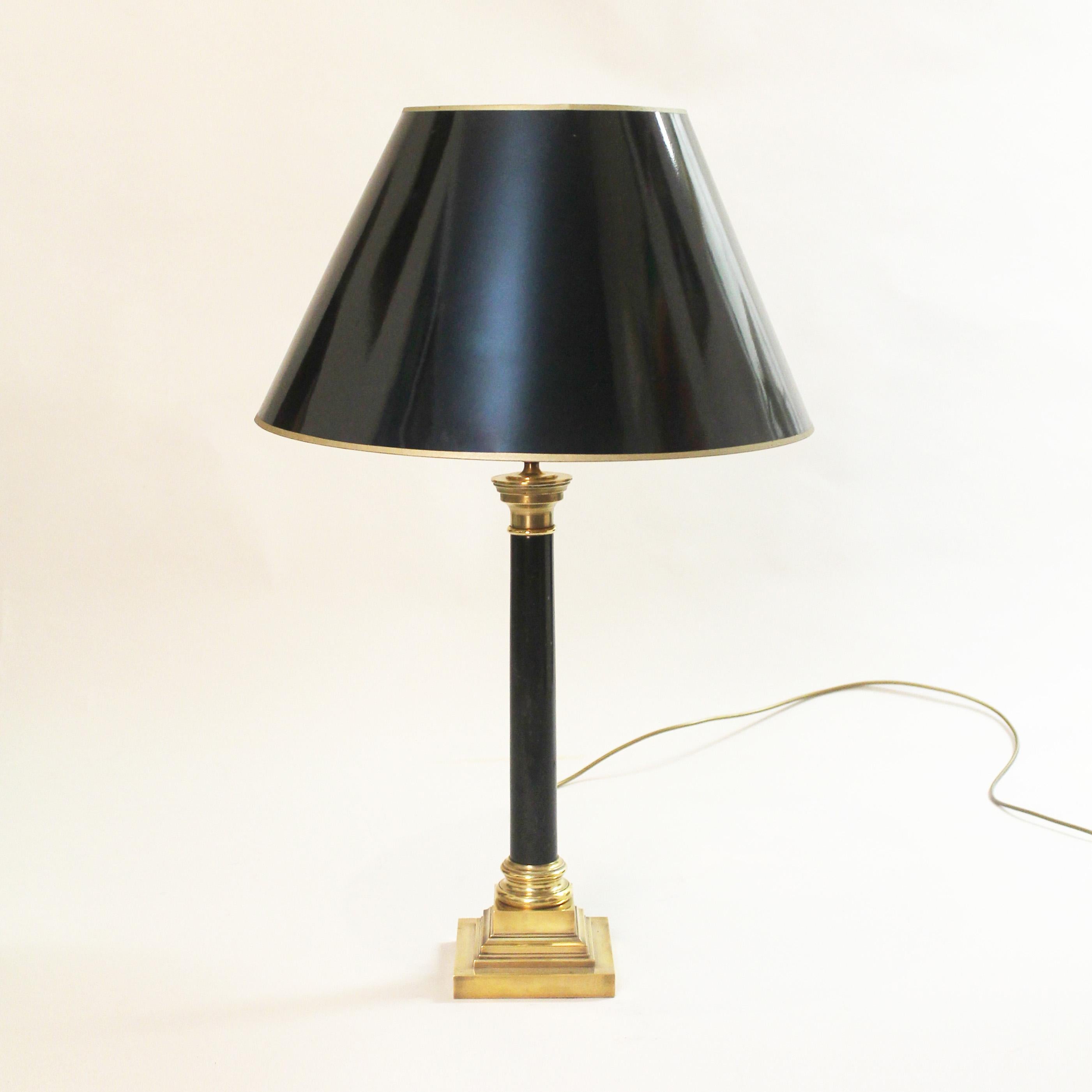 An elegant and statement neoclassical black marble column lamp. The marble column rests on top of a brass stepped base and is topped with a black shade with gold trimming and inner gold lining. All time Classic piece.
