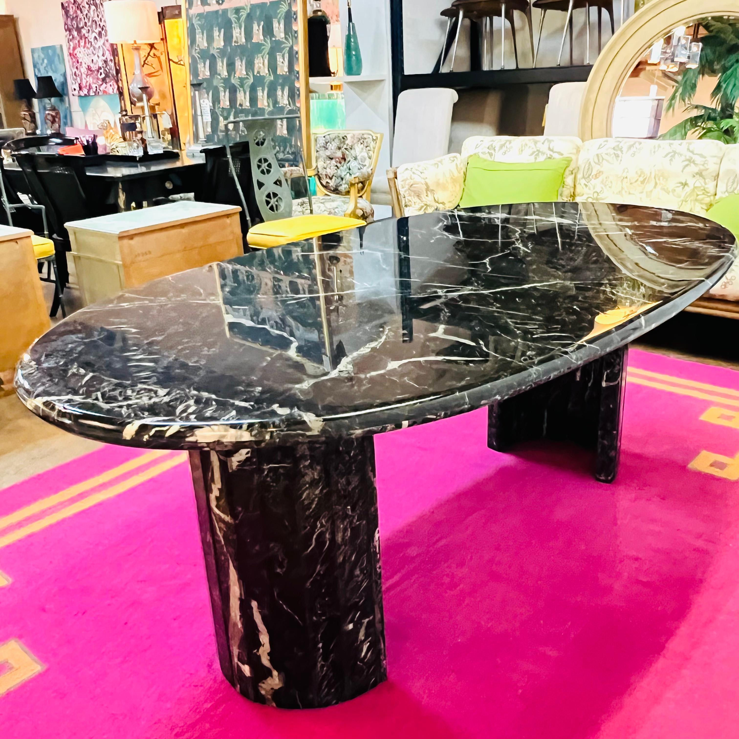 Stunning black marble from top to bottom, this Neoclassical dining table is the ultimate statement piece. A reimagining of the classic double pedestal table, this luxurious piece features two demi-lune beveled pillar legs and a 74