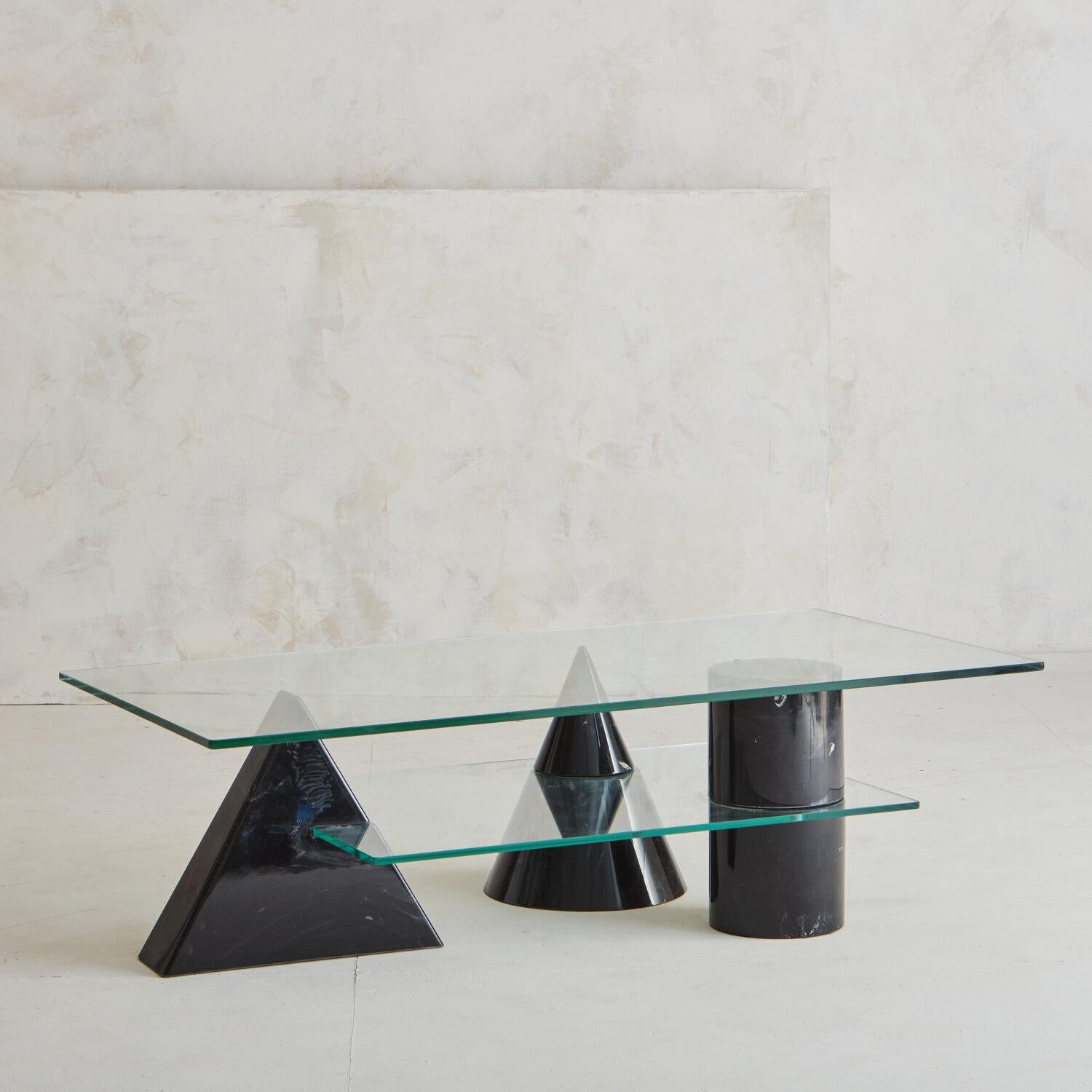 A vintage Italian coffee table featuring 3 Nero Marquina solid marble shapes: a Cylinder, Cone and Pyramid. The three marble shapes support a glass top and a secondary glass shelf. We appreciate the uniqueness of this second glass shelf, which is