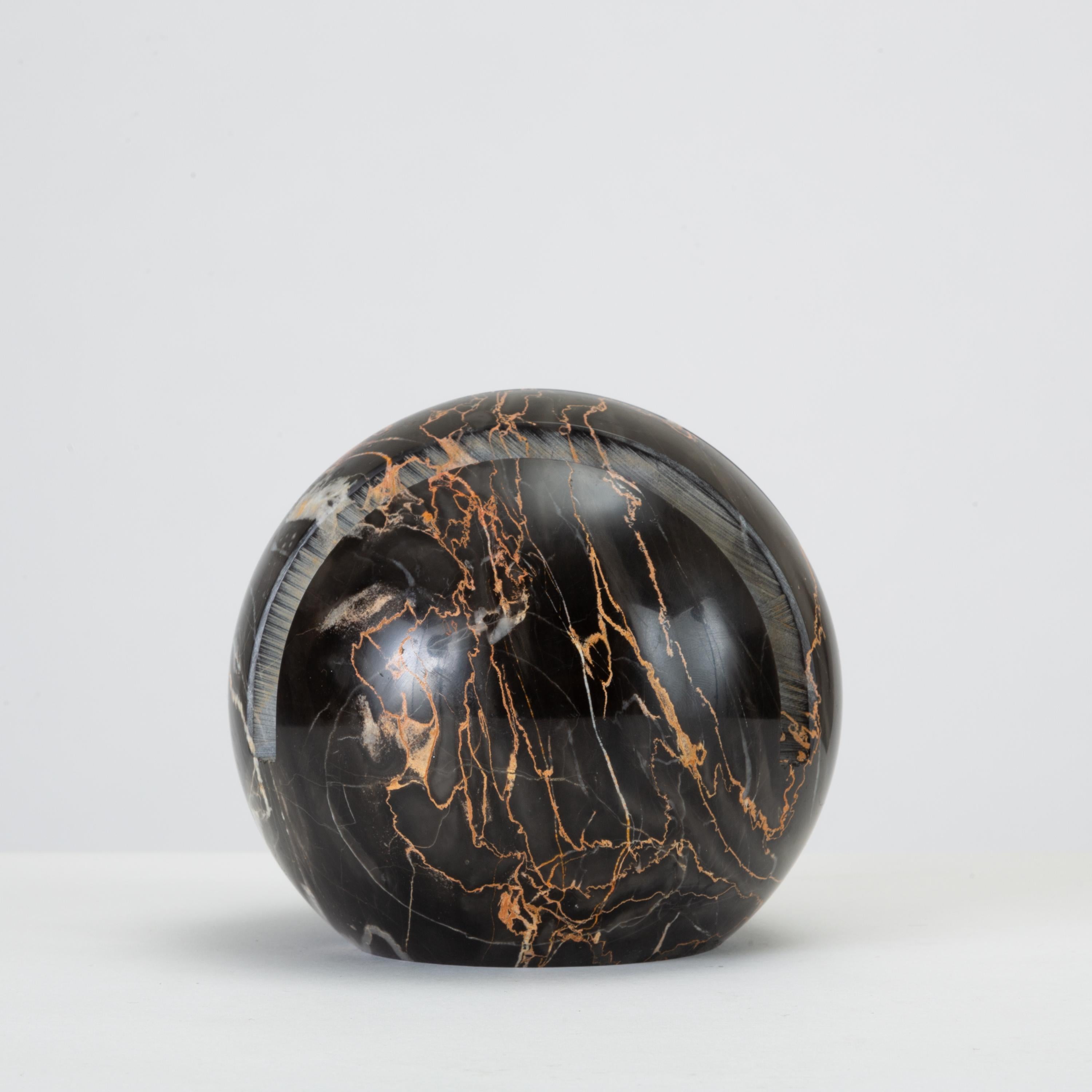 A small desktop mail organizer in black marble. Spherical in shape with a slightly flattened bottom, the piece has four parallel grooves for holding papers. The polished marble is an ebony black with subtle veining in white and salmon pink.