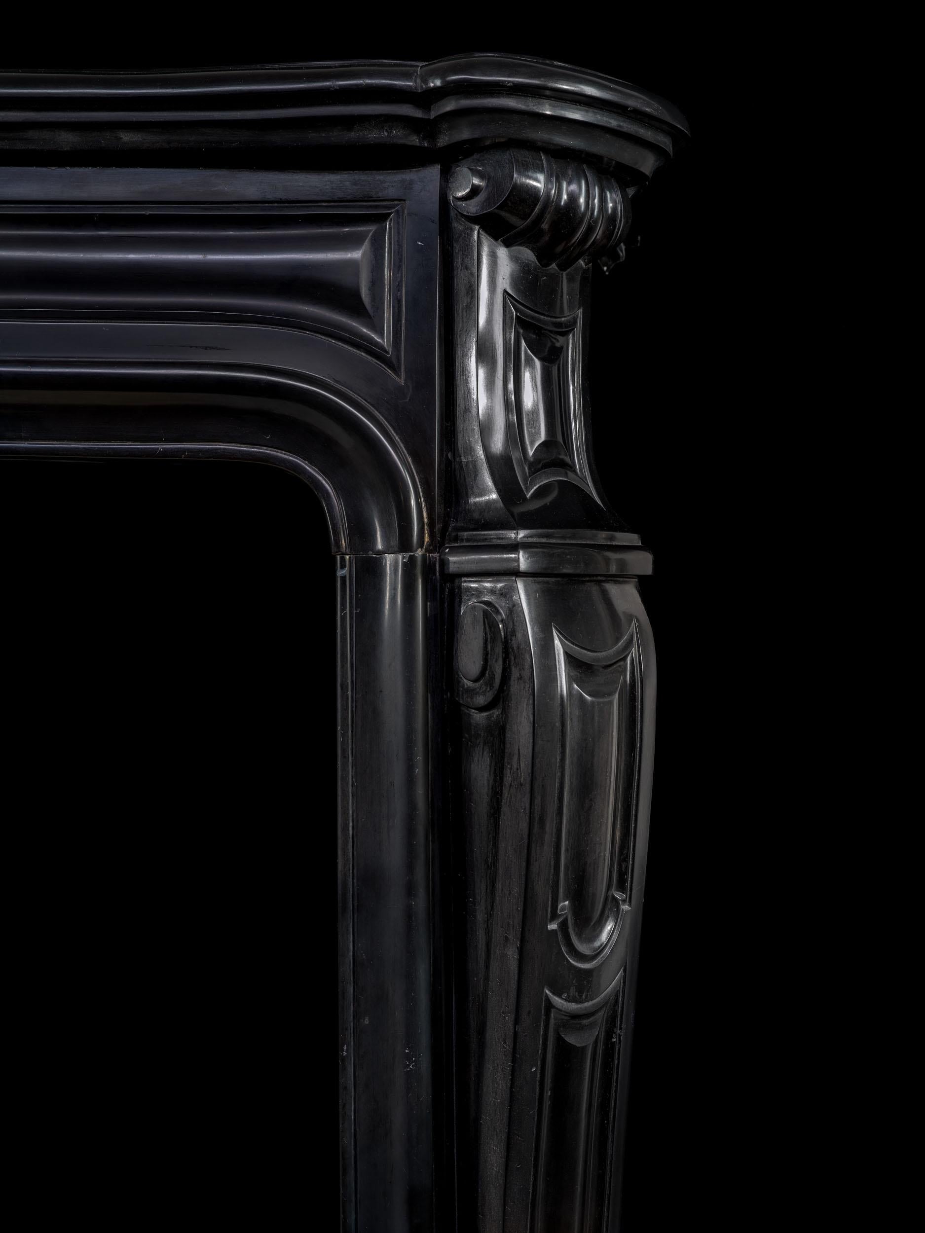Ein antiker Louis XV-Kamin aus schwarzem belgischem Marmor. Dieser auffallend schlichte Kamin hat ein profiliertes Regal über einem getäfelten Fries, das von elegant gekanteten Pfosten getragen wird.

Französisch, Ende 19. Jahrhundert.
