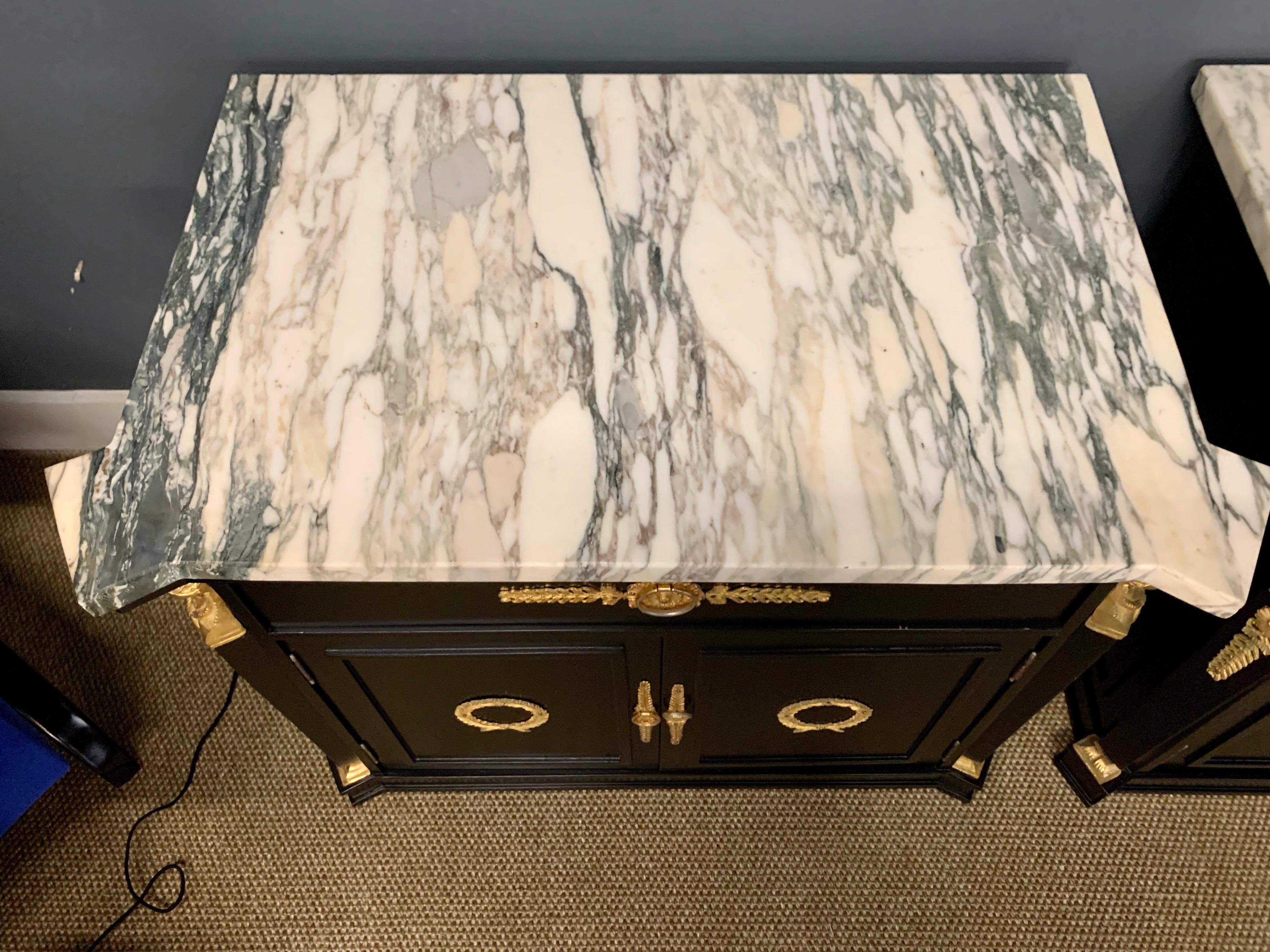 This gorgeous matching set of neoclassical tables have been newly lacquered in black and feature marble tops which are original, one shelf inside each, and green felt for your valuables. The black and gold color scheme makes a great statement in