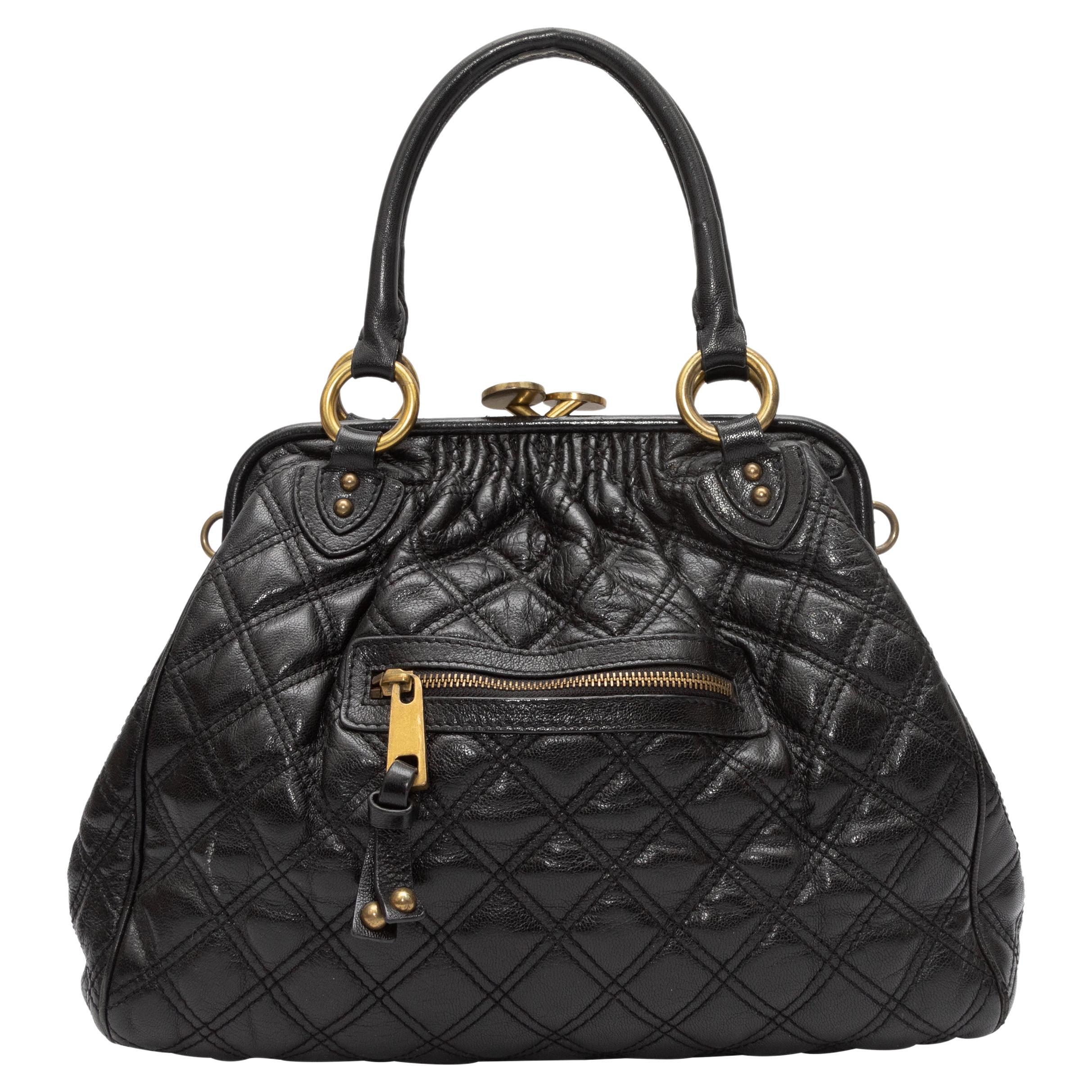 Product Details: Black Marc Jacobs Quilted Leather Stam Handbag. The Stam Handbag features a leather body, gold-tone hardware, burgundy suede interior, an exterior front zip pocket, dual rolled top handles, an optional chain-link strap, and a top