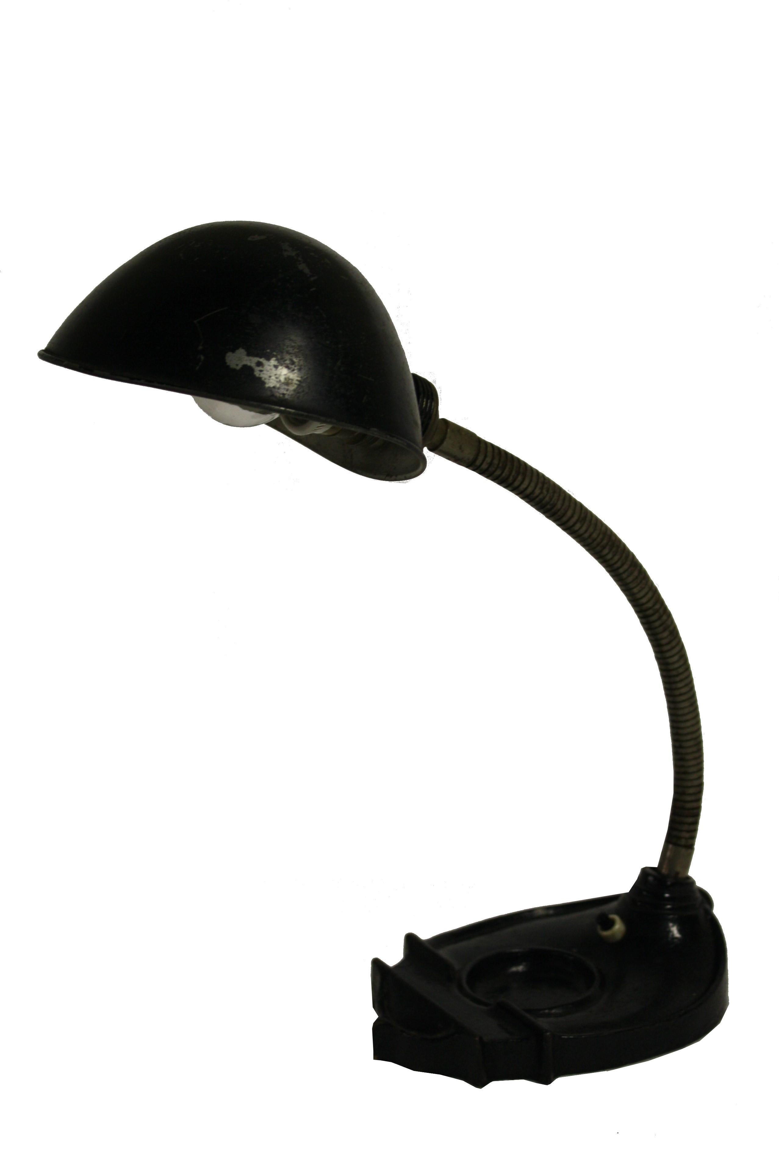 
Art deco era desk lamp with a cast iron base and a black metal shade.

Thanks to it's flexible arm, the lamp is adjustable.

This desk lamp has a typical art deco design with an unusal lamp shade and a base designed to hold a small inkwell and