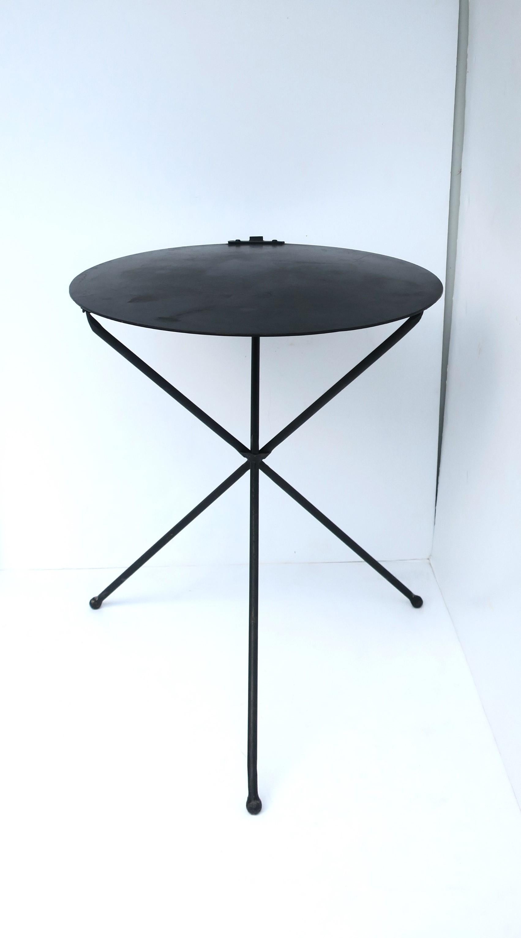 Table d'appoint ou de chevet en métal noir avec plateau circulaire et base tripode, vers la fin du XXe siècle. La table est en métal noirci, solide, a un plateau circulaire sans bord avec des détails de bultes et de boucles/anneaux sur un côté/un