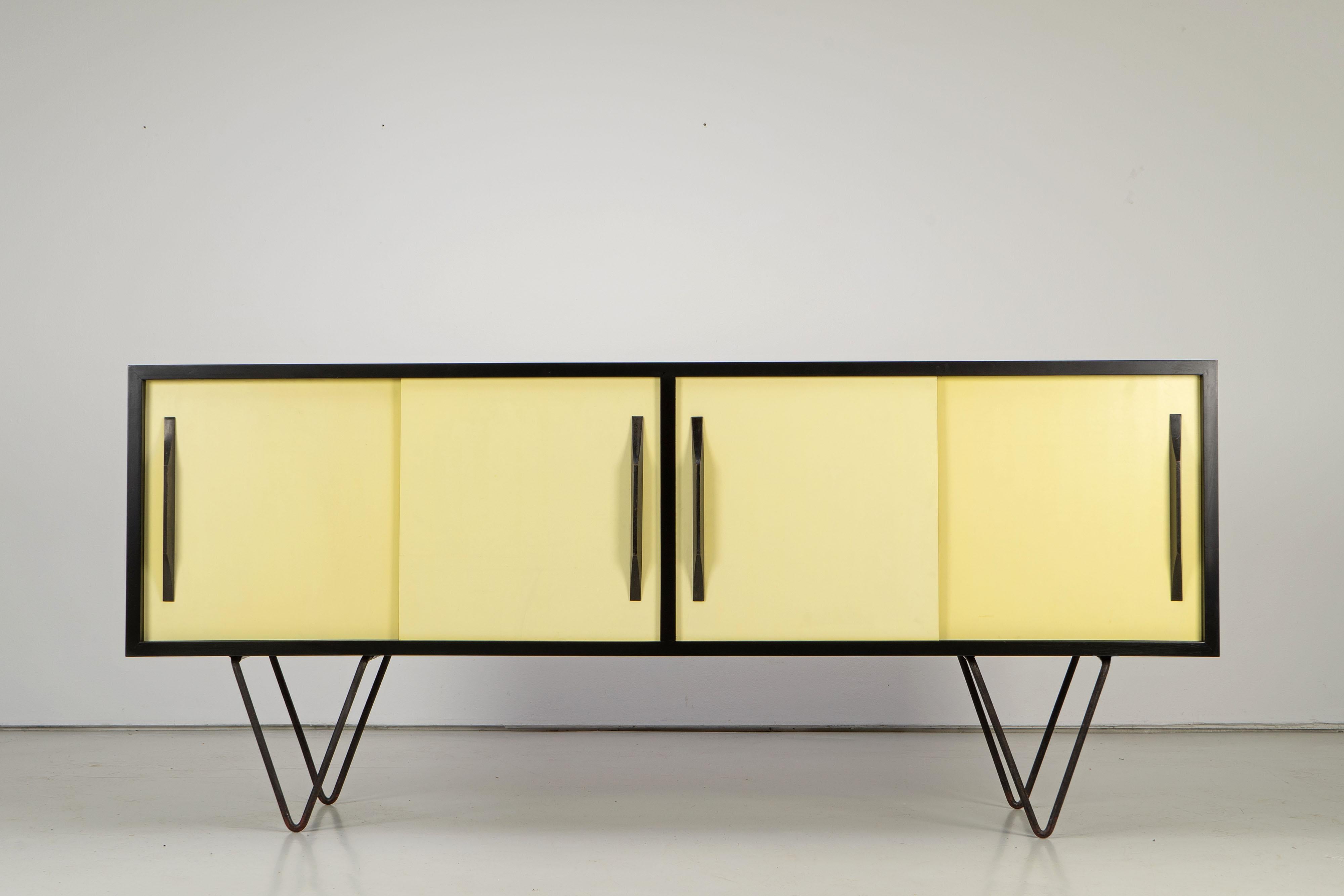 Vintage sideboard on steel feet from the 1950s. Black lacquered body with sliding doors made with faded yellow formica.