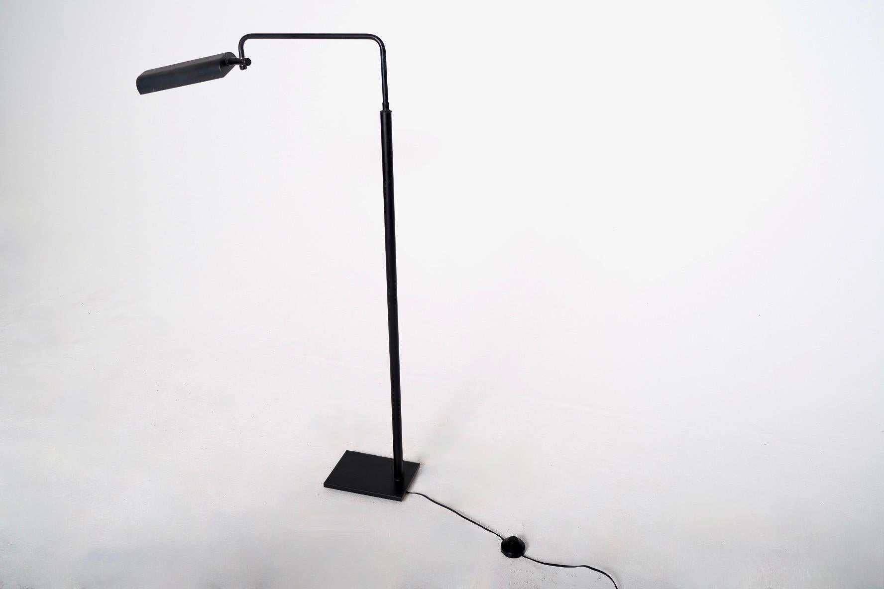 A sleek and refined Italian floor lamp in matte black enamel with a geometric, minimalist silhouette and highly functional design. The lamp features a right-angle arm with a rotating cylindrical head that houses a tubular halogen bulb within a clear