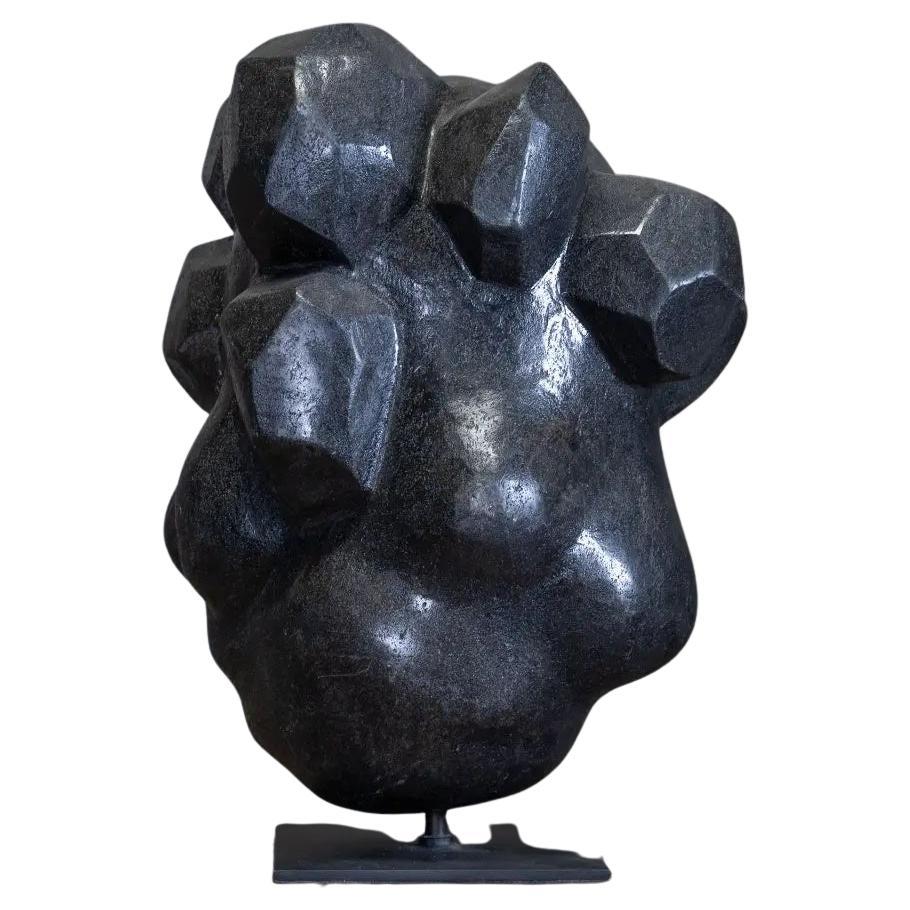 A monolithic sculpture that captures the natural balance of a stack of polished stones. 

This sculpture has an organic, abstract form, combining angular facets and rounded volumes, evoking both a mineral formation and an almost biomorphic mass. It