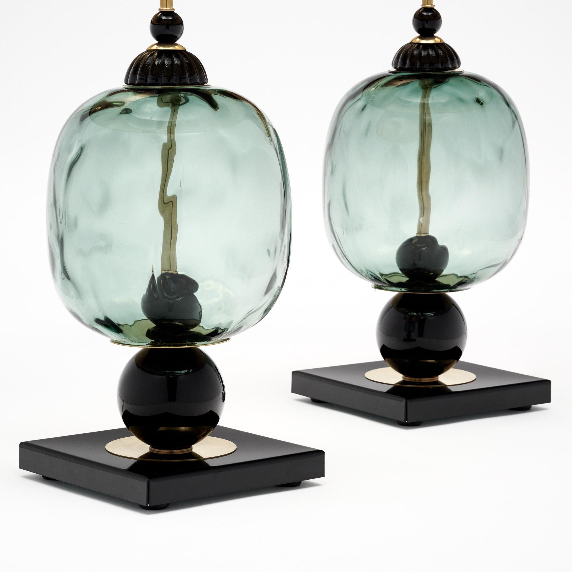 Pair of table lamps made of hand-blown glass elements from Murano, Italy outside of Venice. Each lamp features unique glass components in opaque black and transparent black tones on a brass structure. We love the geometric forms and the combination