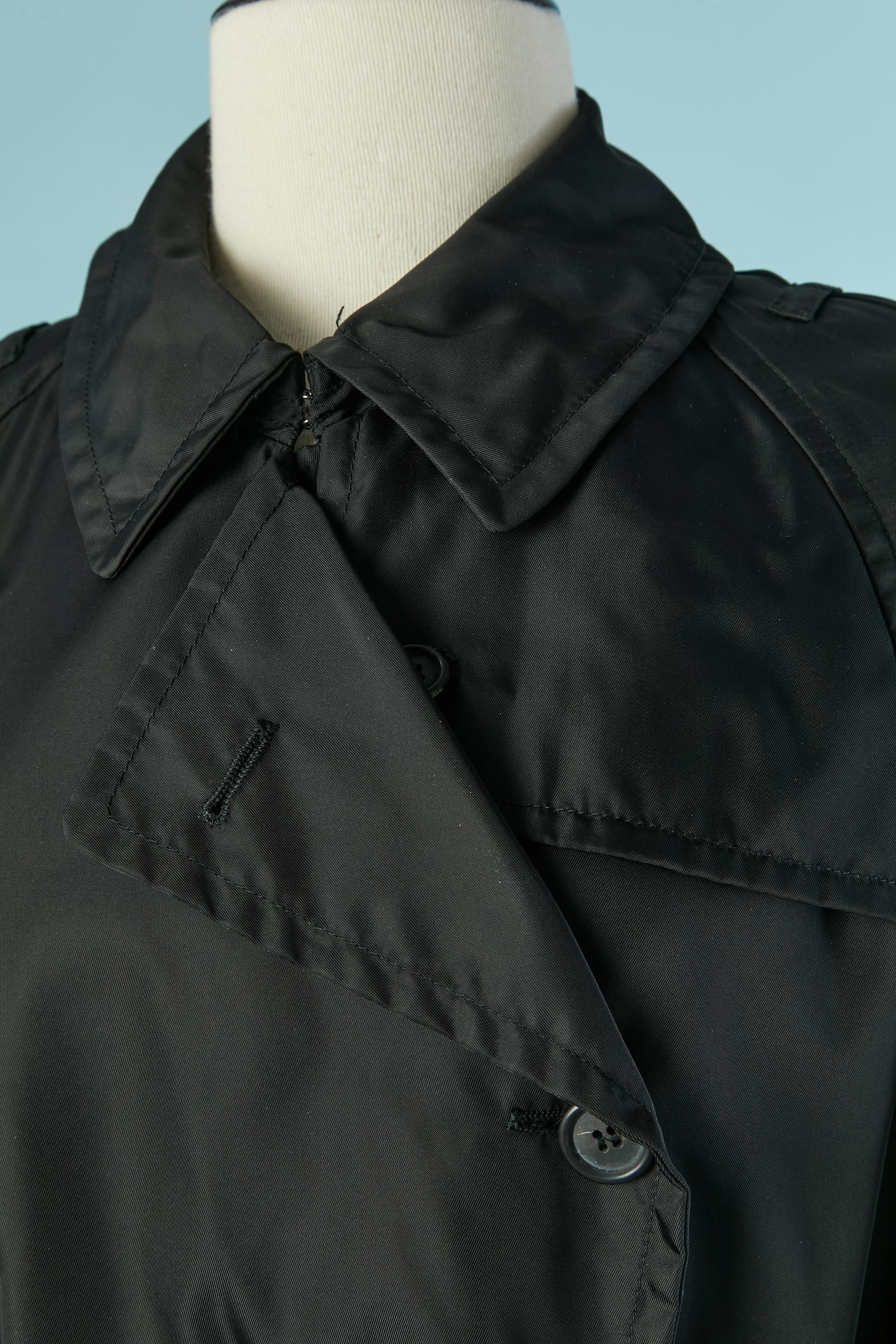 Trench-coat en nylon noir à double boutonnage. Fermeture par boutons et boutonnières sur le devant. Poche sur les deux côtés. Manches raglan. Ceinture avec boucle et passant. 
Taille S sur l'étiquette mais peut aussi aller à M 
