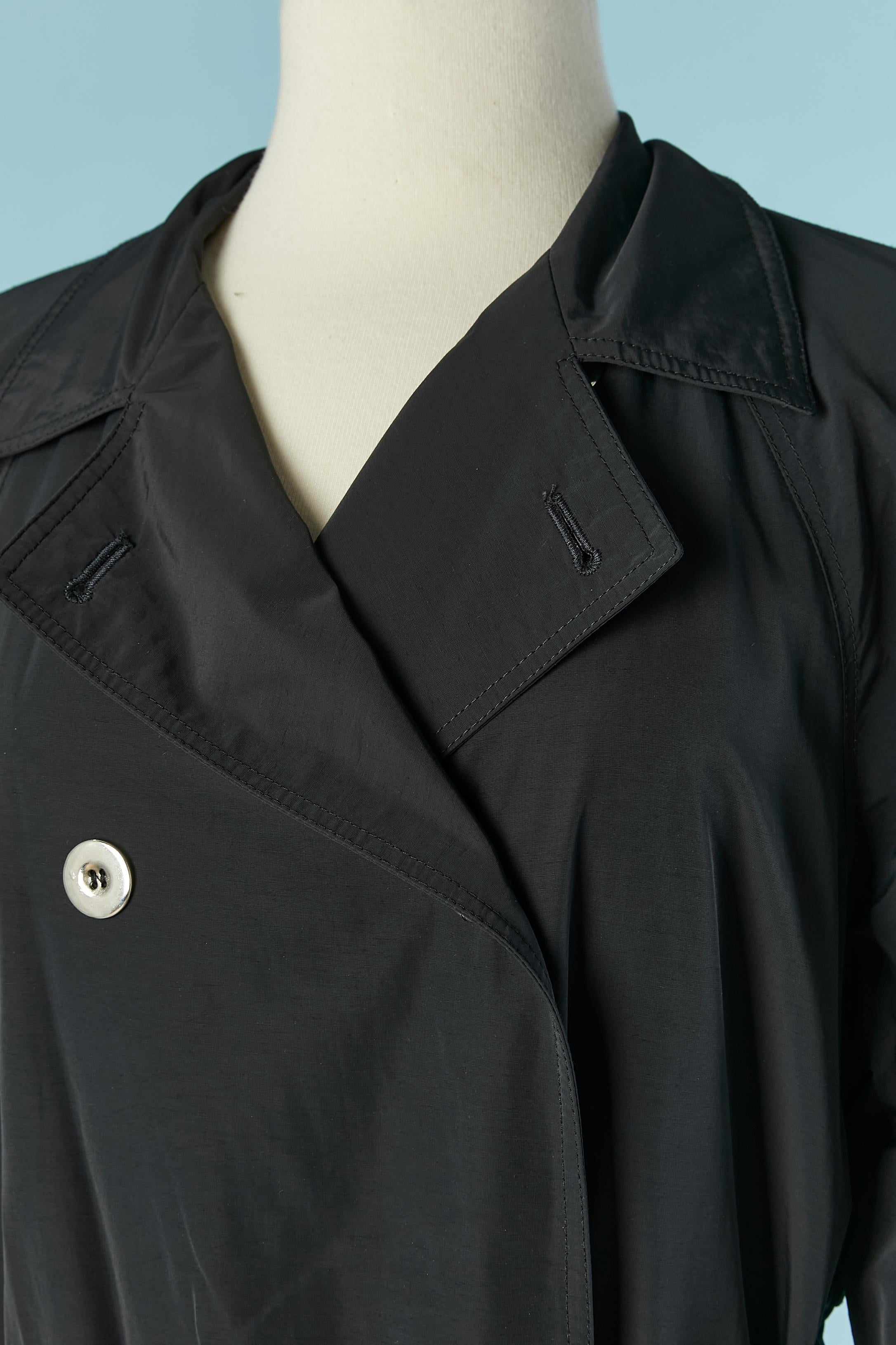 Black nylon trench coat. Shell: 99% polyamide ( nylon) 1% polyurethane. Branded Lining composition: 100% rayon
Pocket on both side. Raglan sleeve. Button and buttonhole closure on the front + on the bottom of the sleeve. Belt, belt-loop and branded