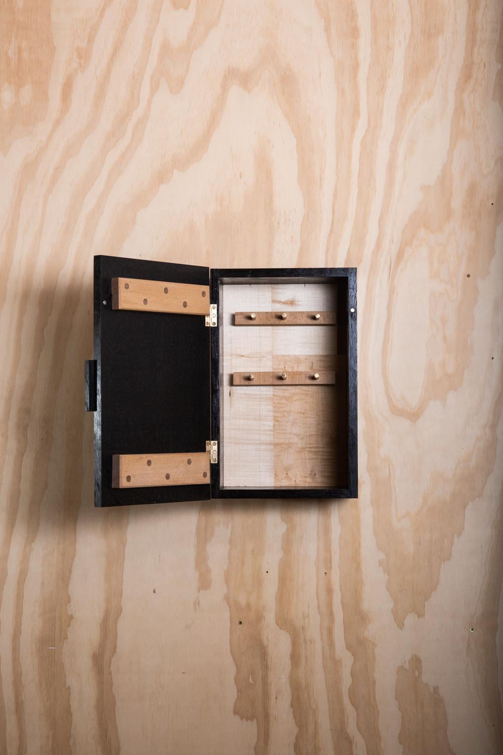Schlüsselkasten aus Eichenholz, mit schwarzer Tinte eingefärbt. Dieser Hängeschrank ist mit seinem Patchwork-Furnier und den Messingdübeln für die Schlüsselhalterung auf der Innenseite wunderbar einzigartig in seinem Design.
Dieser einzigartige und