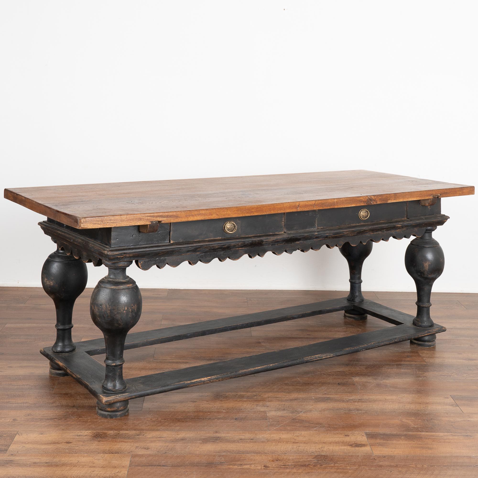 This handsome baroque library table with two drawers has heavily turned legs and a scalloped skirt.
The base has been given a newer, professionally applied black finish and is lightly distressed revealing the natural wood below while complimenting