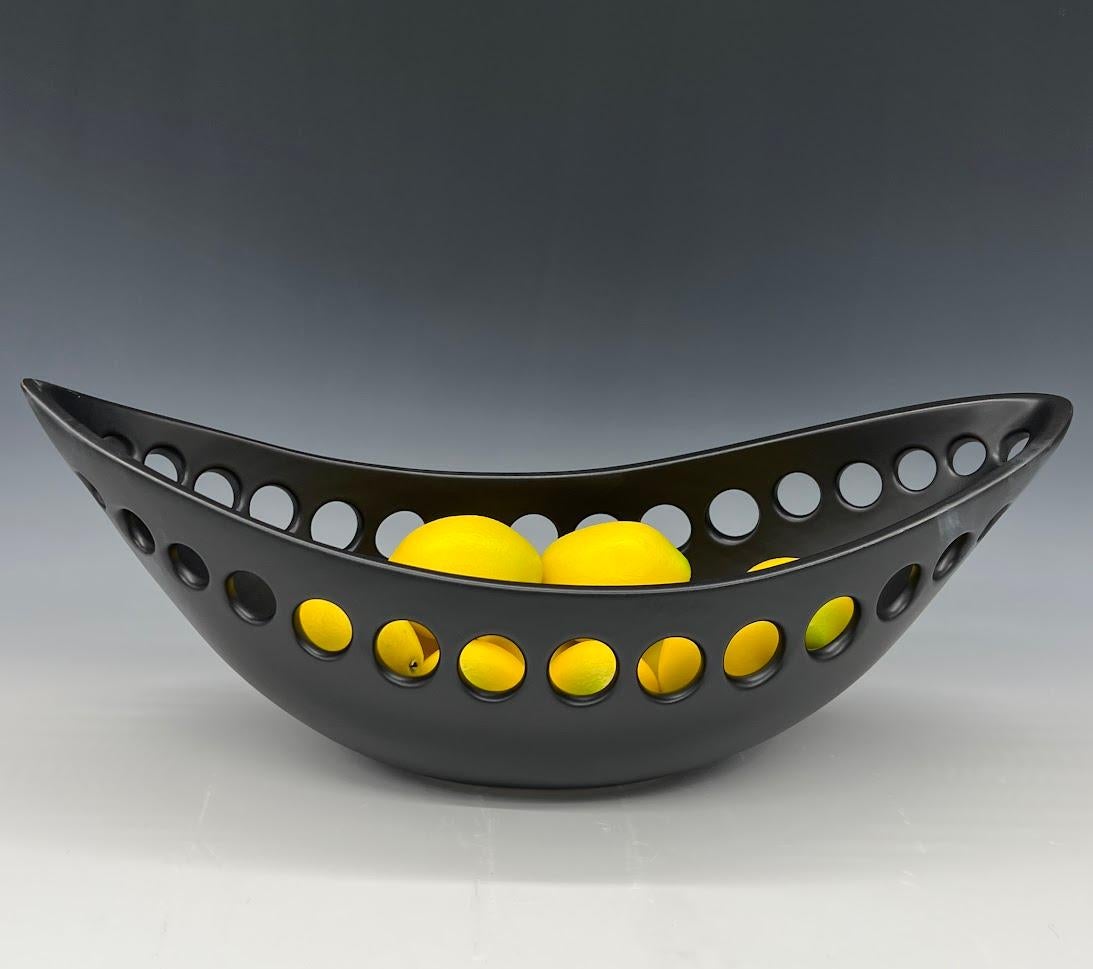 Inspired by organic contemporary design, this pierced oblong bowl is wheel thrown, distorted and hand pierced stoneware with a black satin glaze. Small holes are created when the clay is still wet and then each hole is painstakingly enlarged and