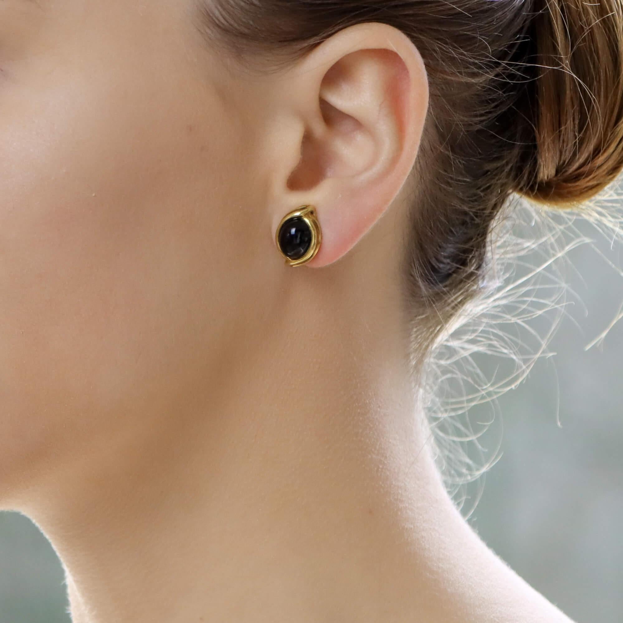 An elegant pair of black onyx cabochon clip-on earrings set in 18k yellow gold. 

Each earring features an oval cabochon black onyx stone which is set within a fancy ridged yellow gold border. The earrings are secured to reverse with secure omega