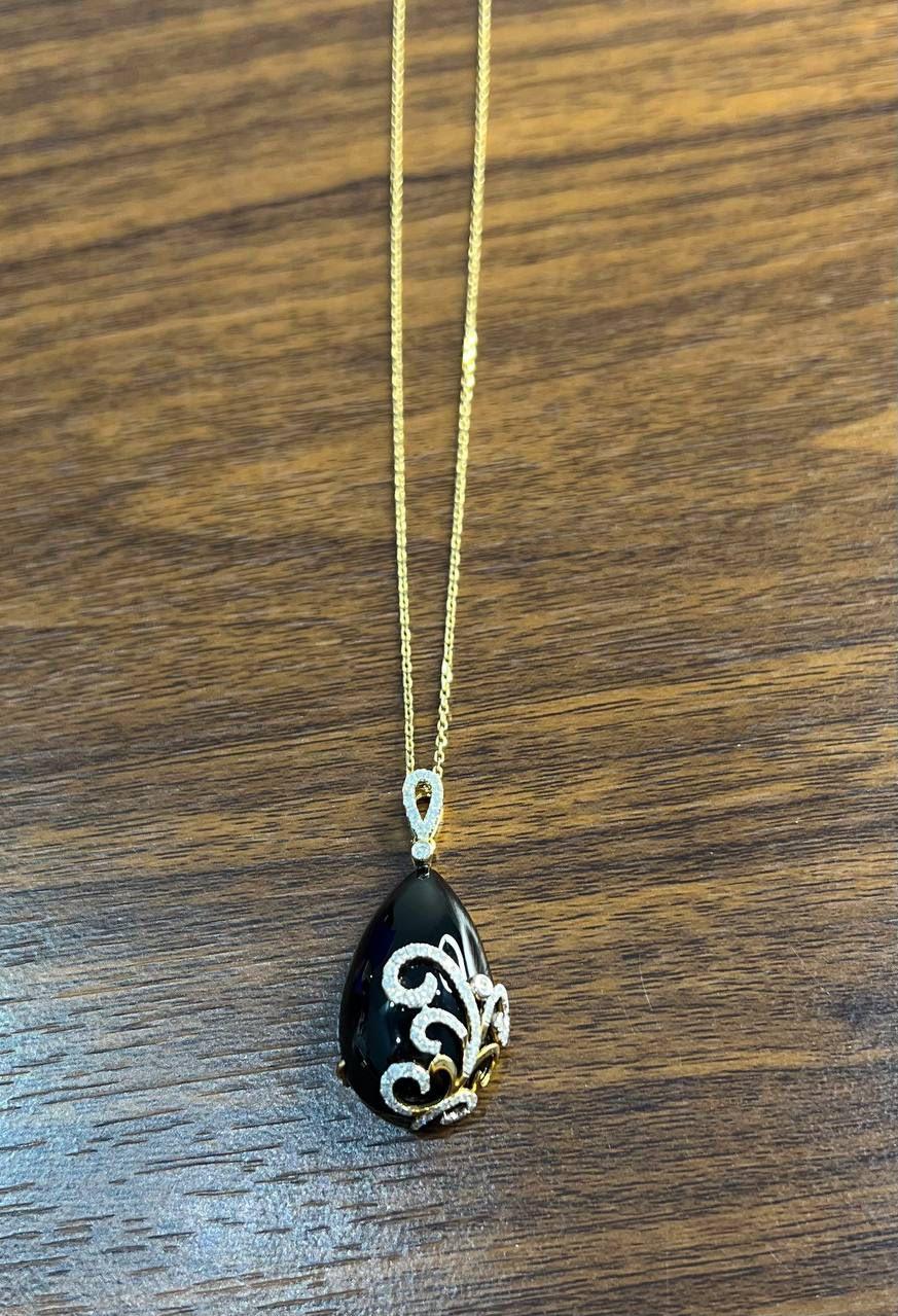 This exquisite pendant necklace is finely crafted with a teardrop-shaped black onyx. The pendant is adorned with intricate scrollwork, encrusted with sparkling diamonds of G/VS Quality White Diamonds. Diamond accents the bail, adding elegance to the