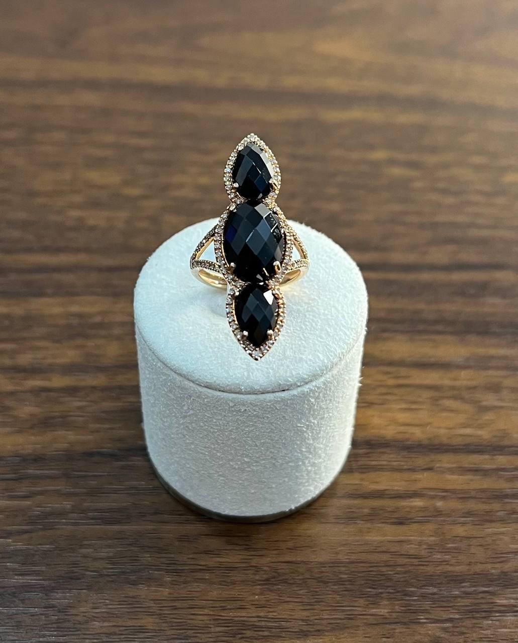 Un llamativo anillo con tres ónices negros facetados, elegantemente engastados en disposición vertical. Cada piedra está rodeada por un delicado halo de diamantes, que realza su profundo matiz. El engaste es de oro de 14 quilates, lo que proporciona