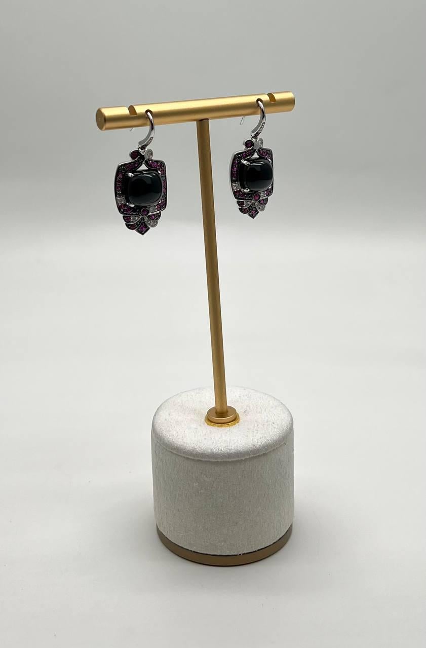 Exquisite and bold, these striking earrings feature a captivating design with dark, glossy central black onyxes surrounded by a halo of vibrant pink red rubies. The intricate arrangement forms a unique, eye-catching silhouette. Modern elegance in