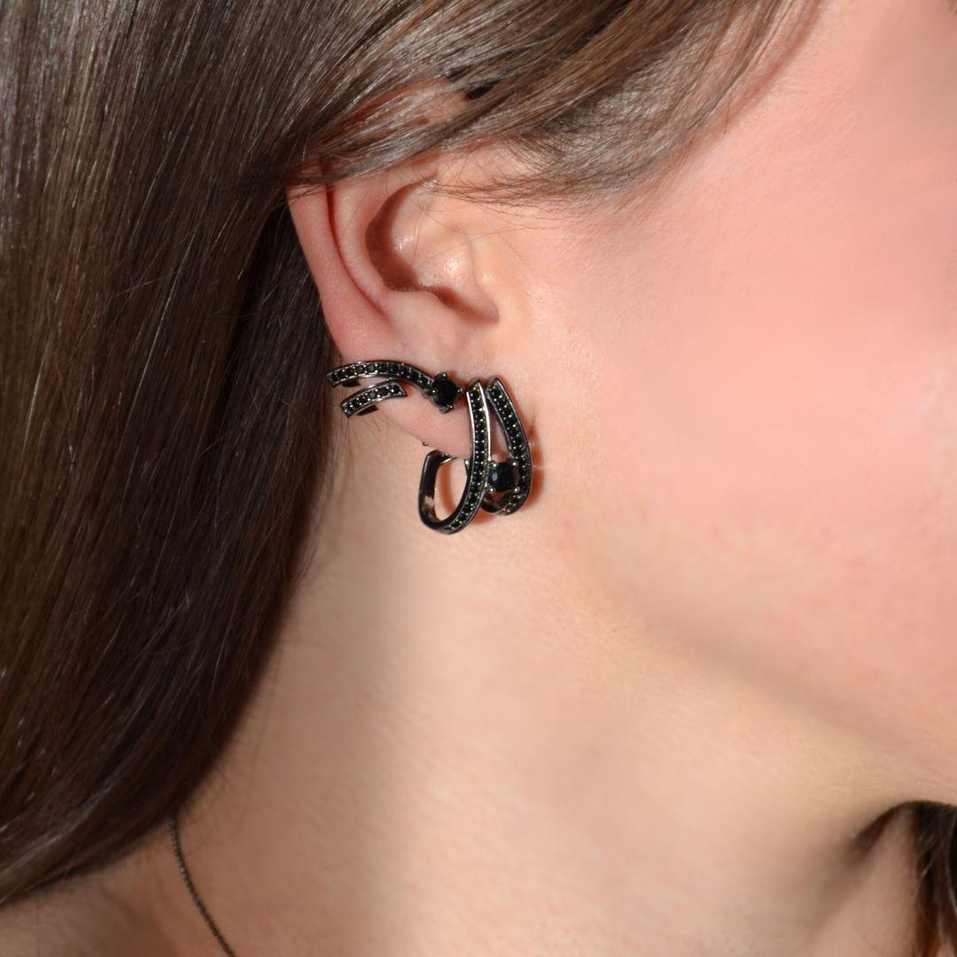 Fai una dichiarazione audace con questi orecchini dal design astratto, con gemme di onice nero e spinello nero elegantemente incastonate nell'argento 925. Rifiniti con un lussuoso rodio nero, gli orecchini vantano un design unico e scultoreo che