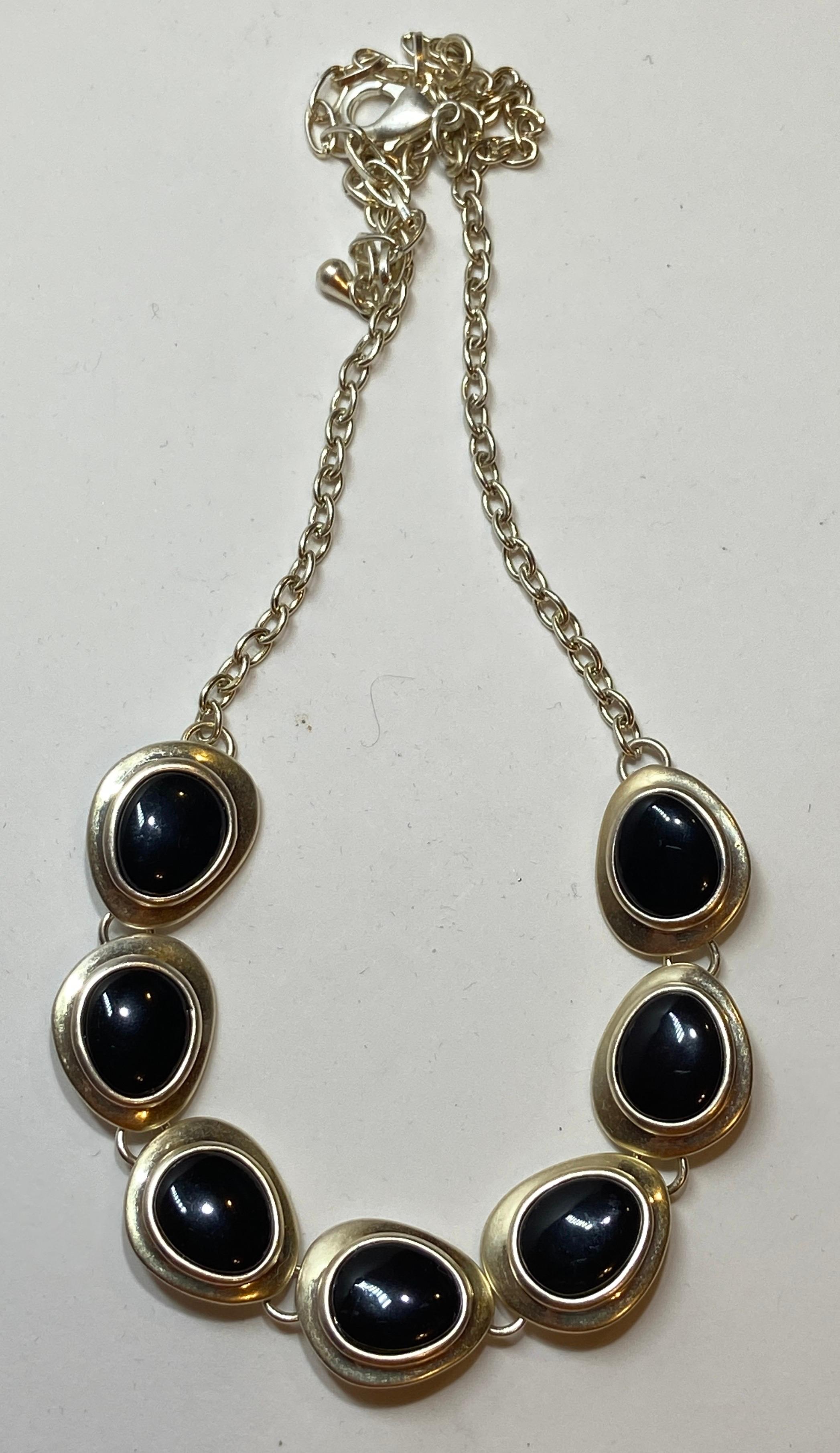 This wonderfully simple yet elegant black onyx surrounded with sterling silver is shaped like gentle soft-like pebbles. The chain-link necklace is of brushed silver hardware. Made in US.