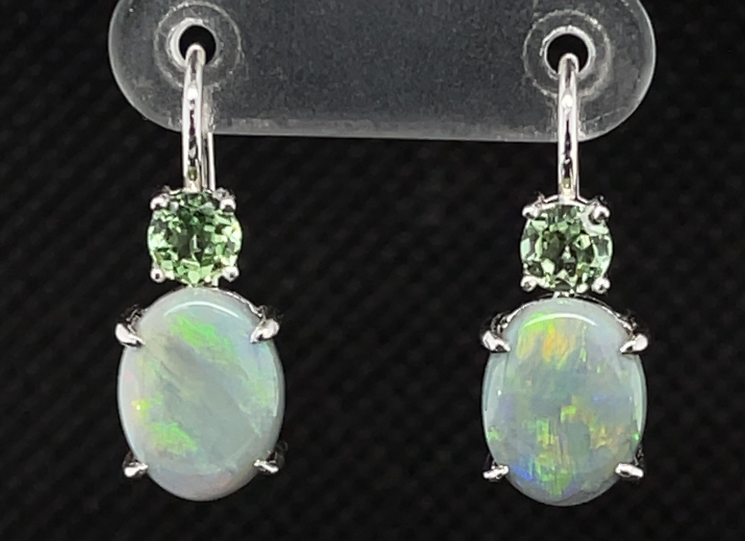 The color pairing of semi-black opals with pastel green overtones and pastel tsavorite garnets of the same color of green is both subtle and beautiful. They are cool color tones that we have set in 18k white gold handmade lever-back earrings. Oval