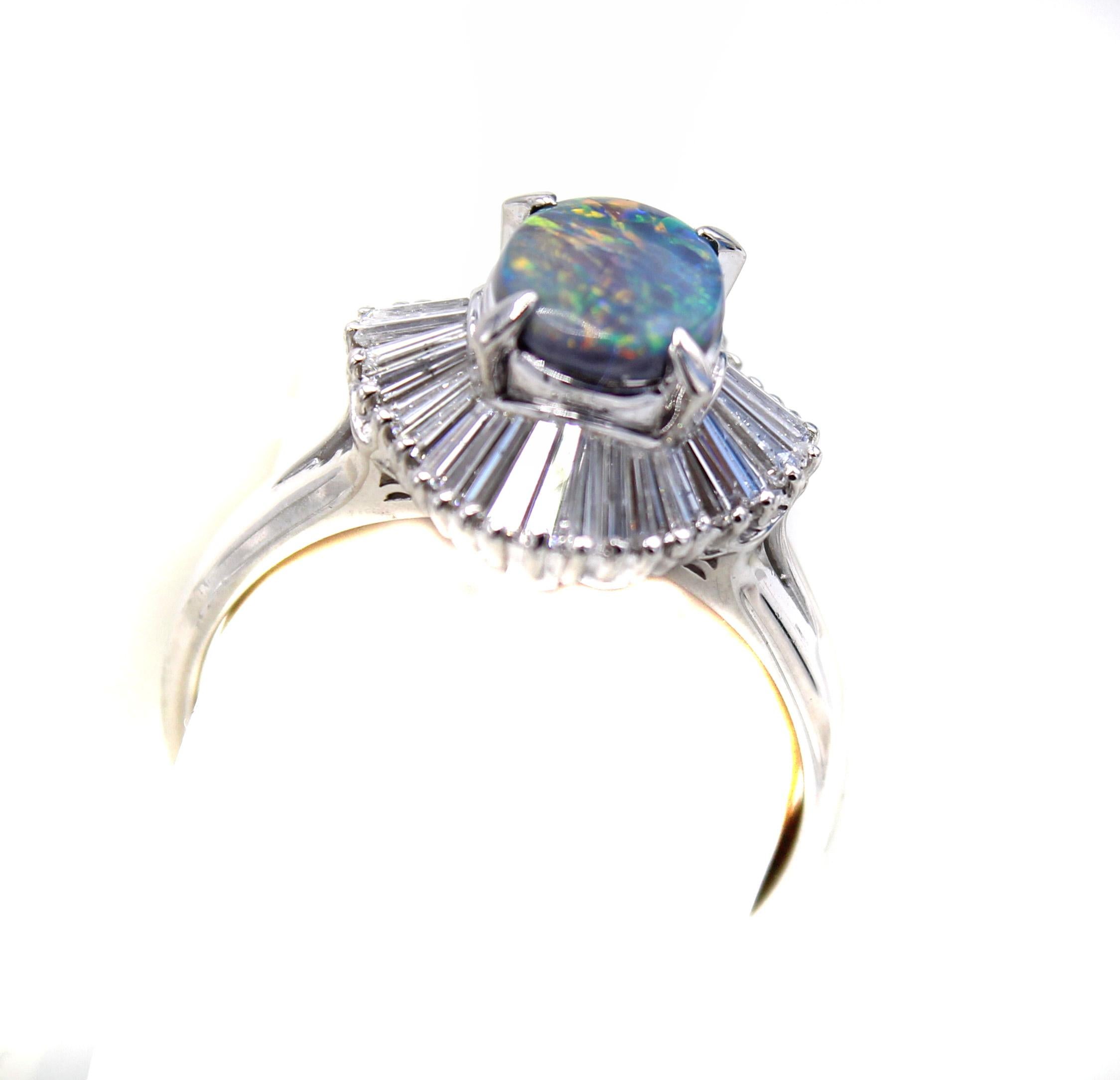 Beautifully designed and wonderfully hand-crafted this 1970s ring features an oval black opal surrounded by bright white tapered baguette cut diamonds. The black opal displays an amazing amount of red, along with blue, green and orange. The