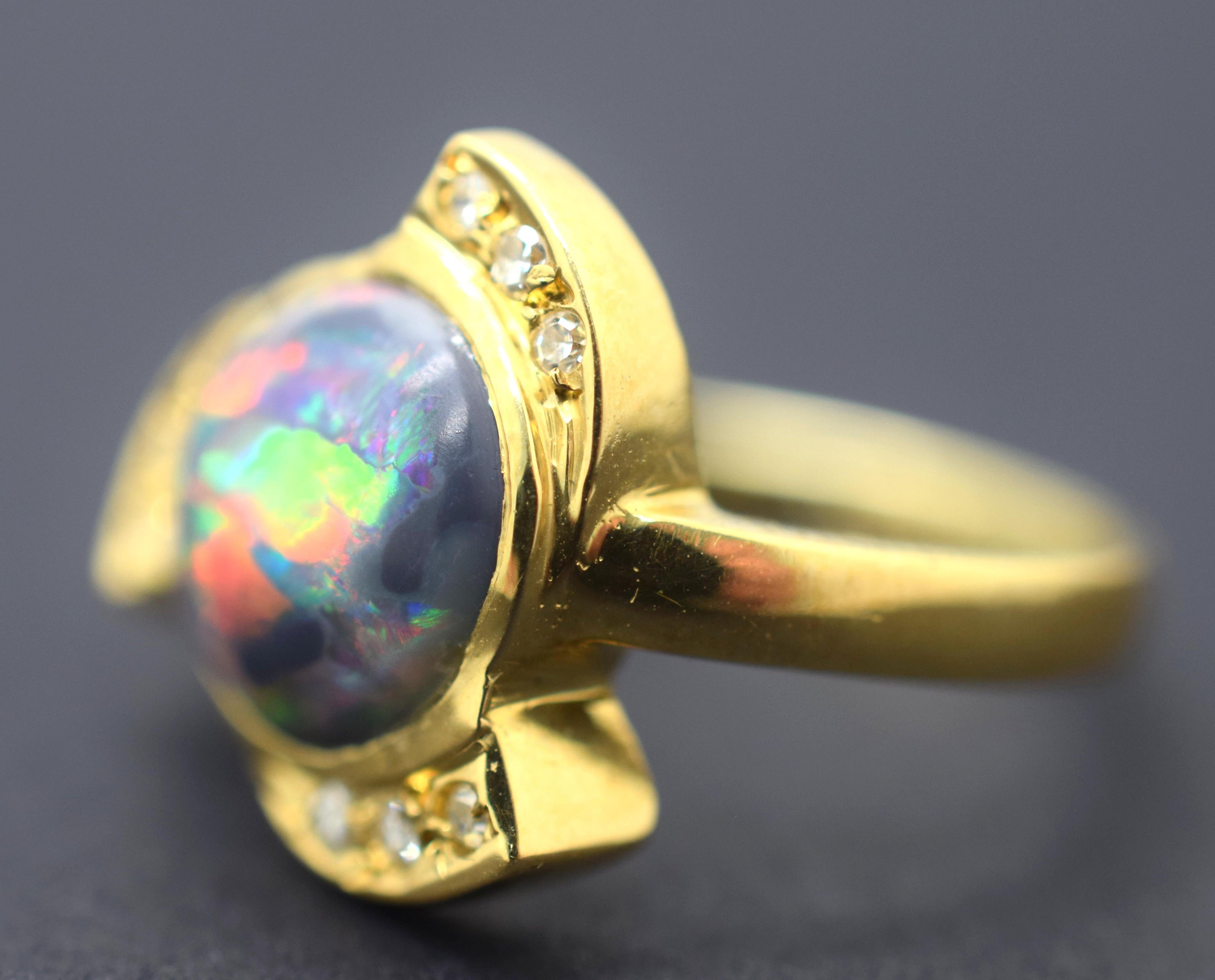 Fantastic estate Black Opal and Diamond Ring. This ring is crafted in 18k yellow gold. The focal point of the ring is a cabochon Black Opal with  beautiful play of color. Red, green and blue flash across this ring with an electric display of colors.
