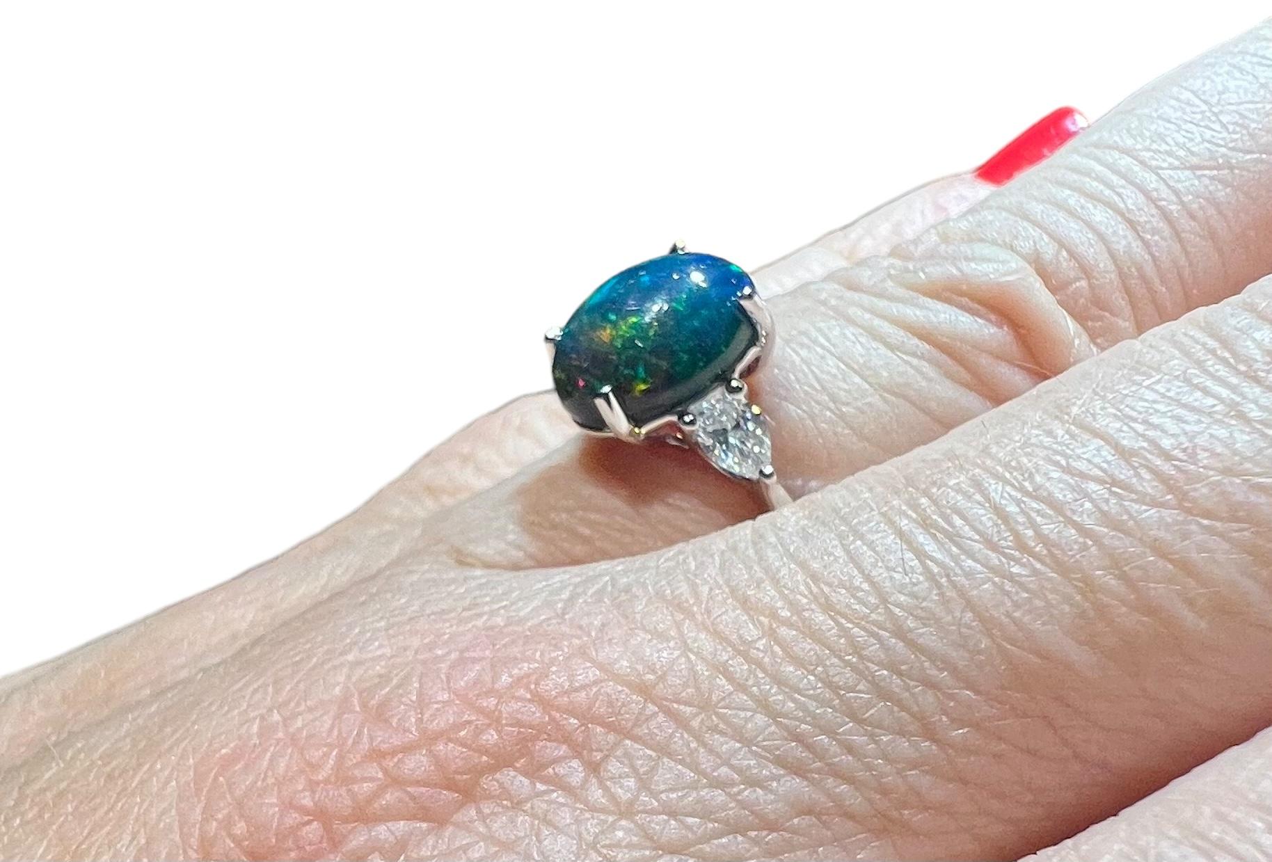 Beautiful cabochon-cut black opal,
with superb bright fires ranging from pink to red, blue to violet, yellow to green,  
The black opal weighs 2.30 carats,
it is set with two pear-shaped diamonds totalling 0.38 carat, 
on an 18-carat white gold ring