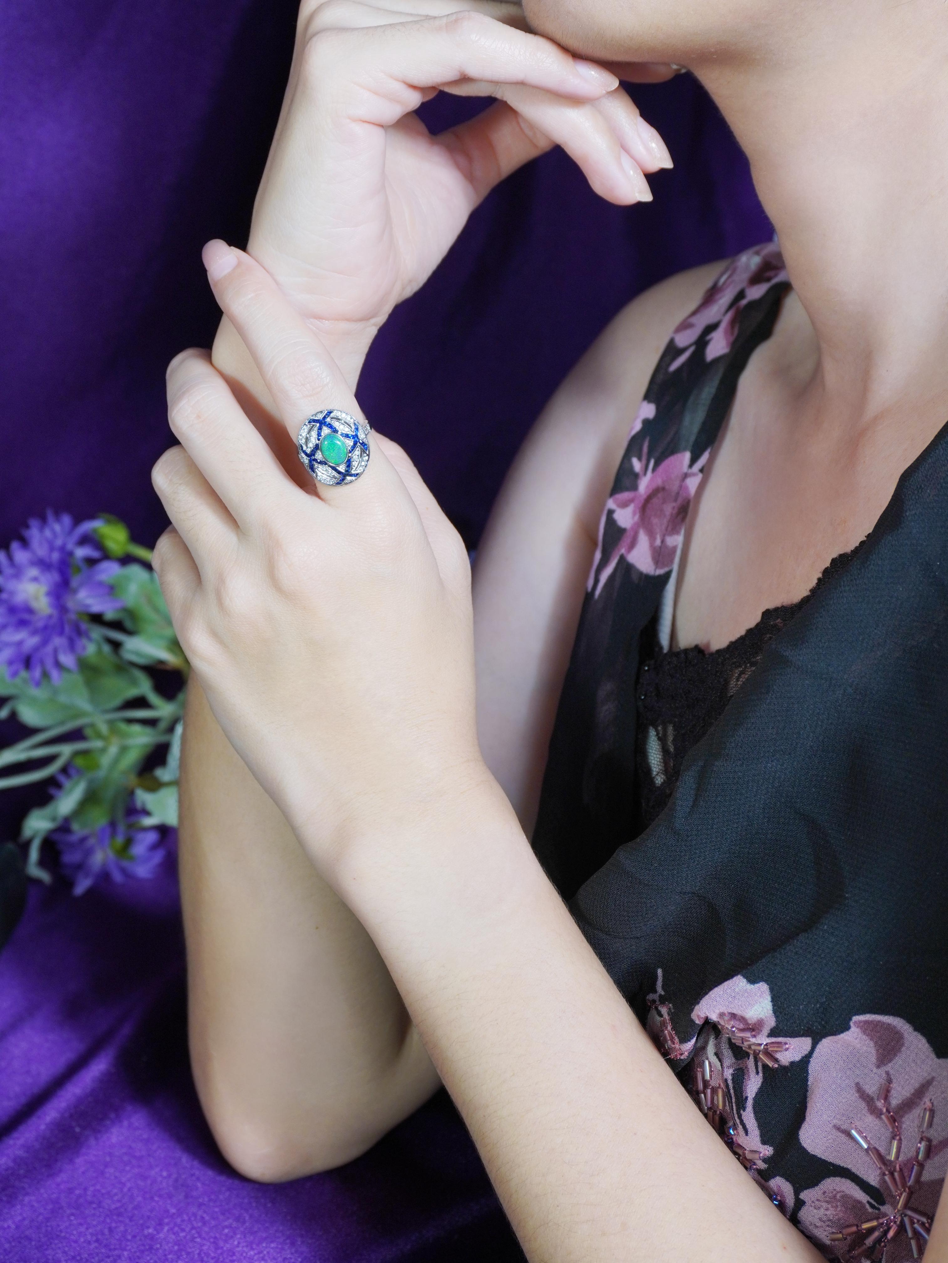 Captez la beauté mystérieuse avec cette bague cocktail de style Art déco en opale noire, saphir et diamant. En son cœur se trouve une opale noire envoûtante, rayonnant de couleurs profondes et changeantes. Autour de lui, des diamants et des saphirs