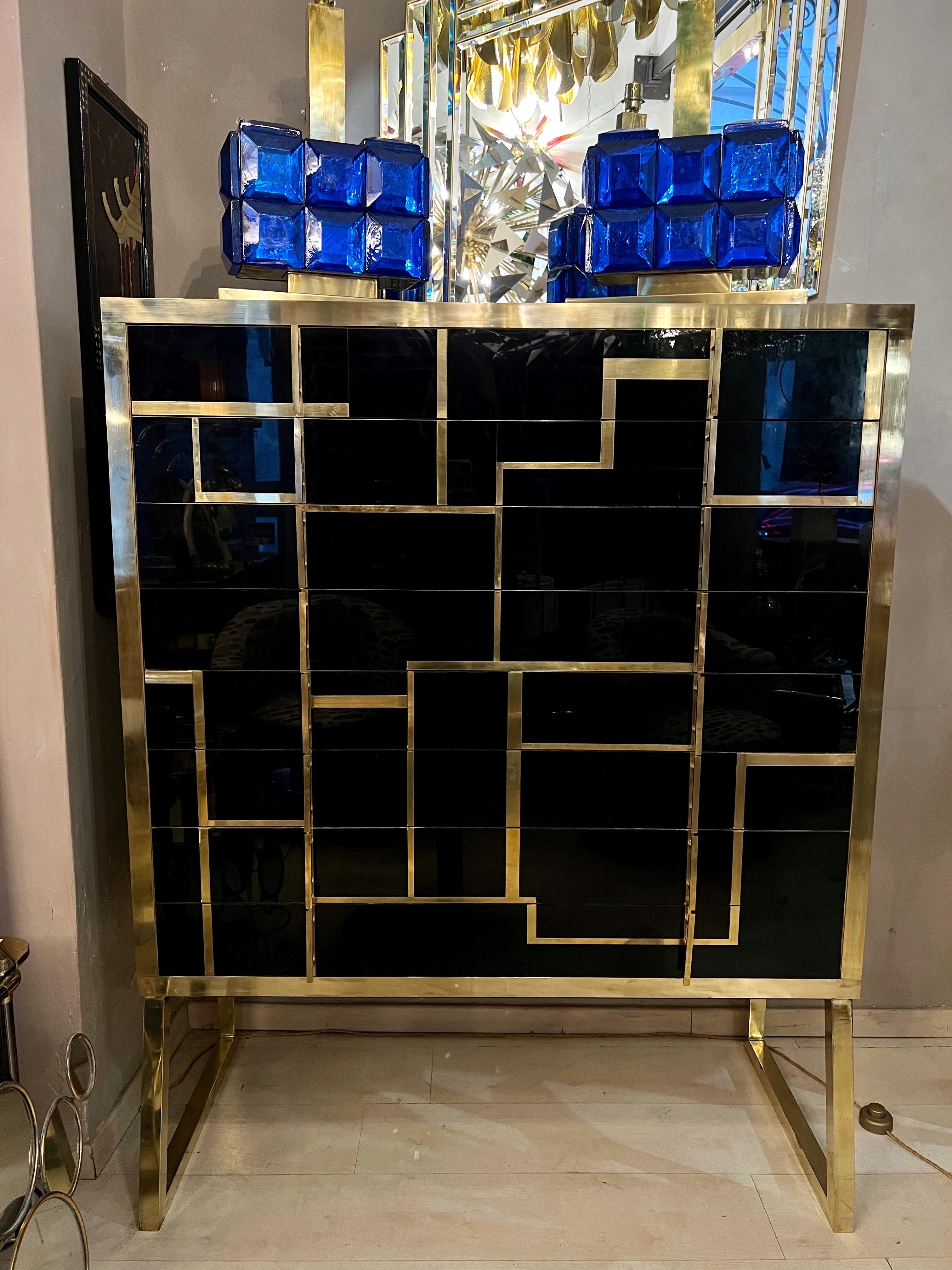 Black opaline glass high chest of drawers with brass and gold opaline glass inserts.
The chest has brass handles and legs and 8 drawers.