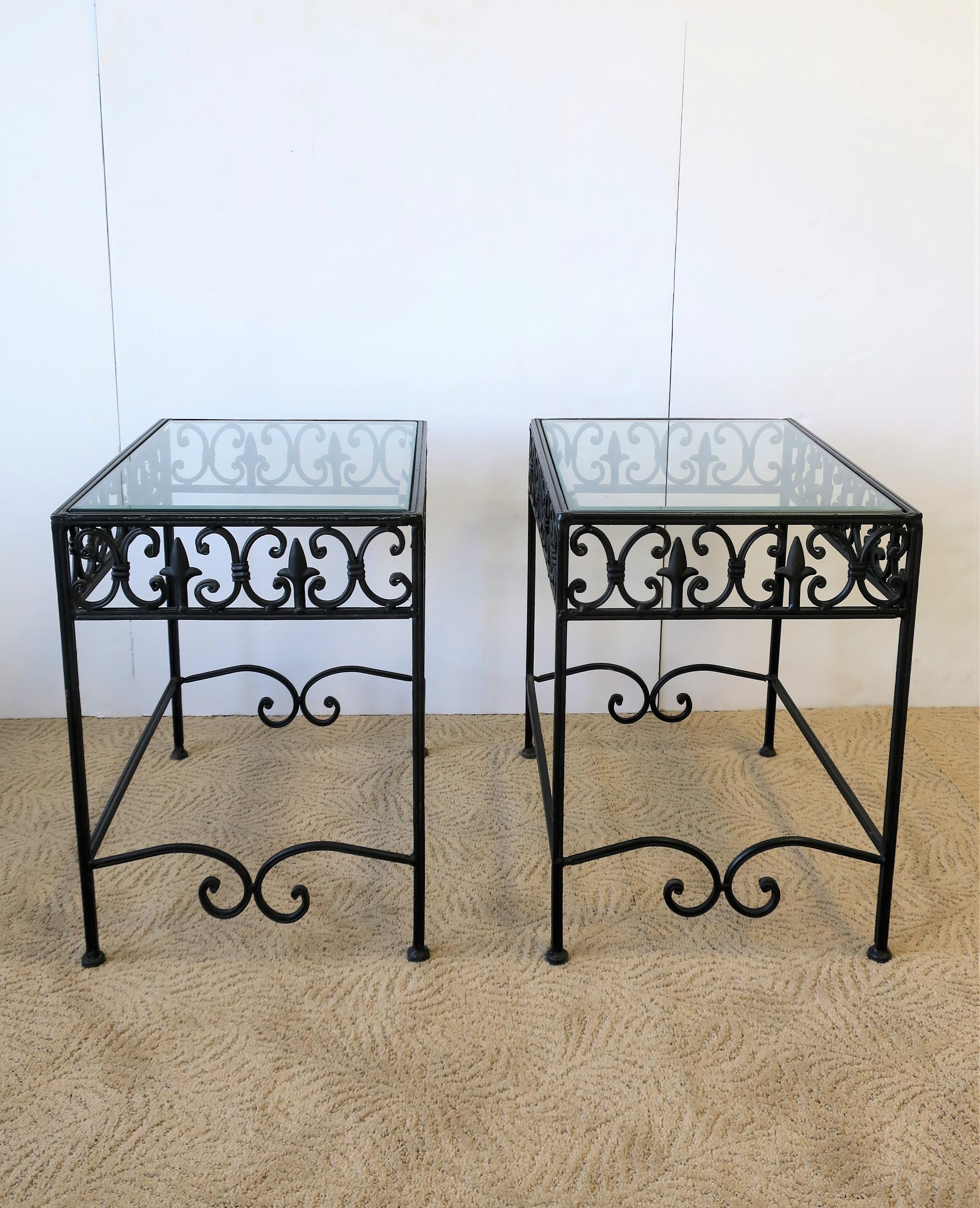 A beautiful and substantial pair of outdoor patio/terrace/garden rectangular black metal and glass end tables with a 'fleur-de-lis' type design, circa late 20th century. Glass tops have beveled edge and sit 'inset' into table bases, with no glass
