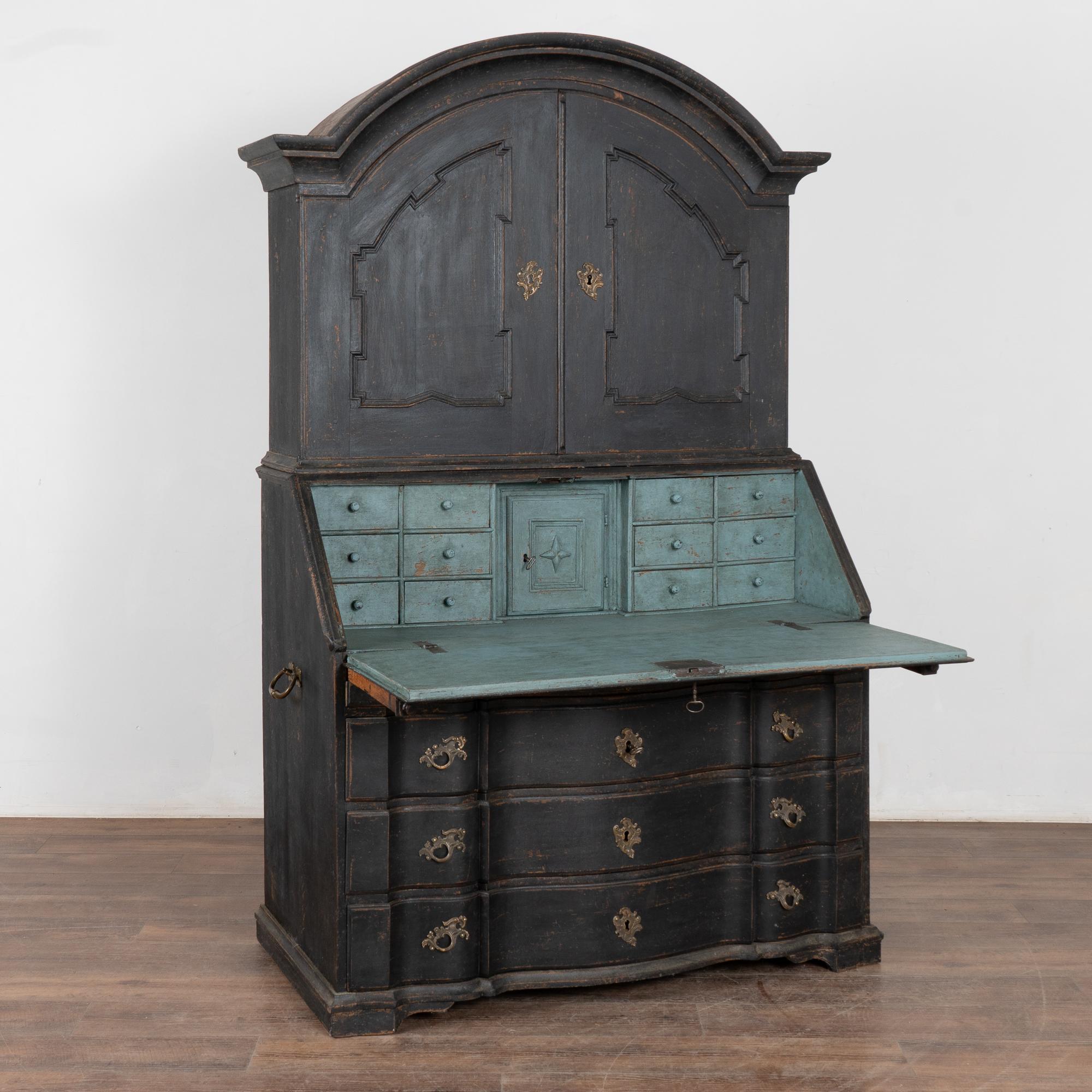 This striking oak secretary is an elegant statement piece crowned with a curved bonnet. Note the heavily carved panel doors and the large curvaceous lower three serpentine drawers.
The entire secretary has been given a professional custom layered