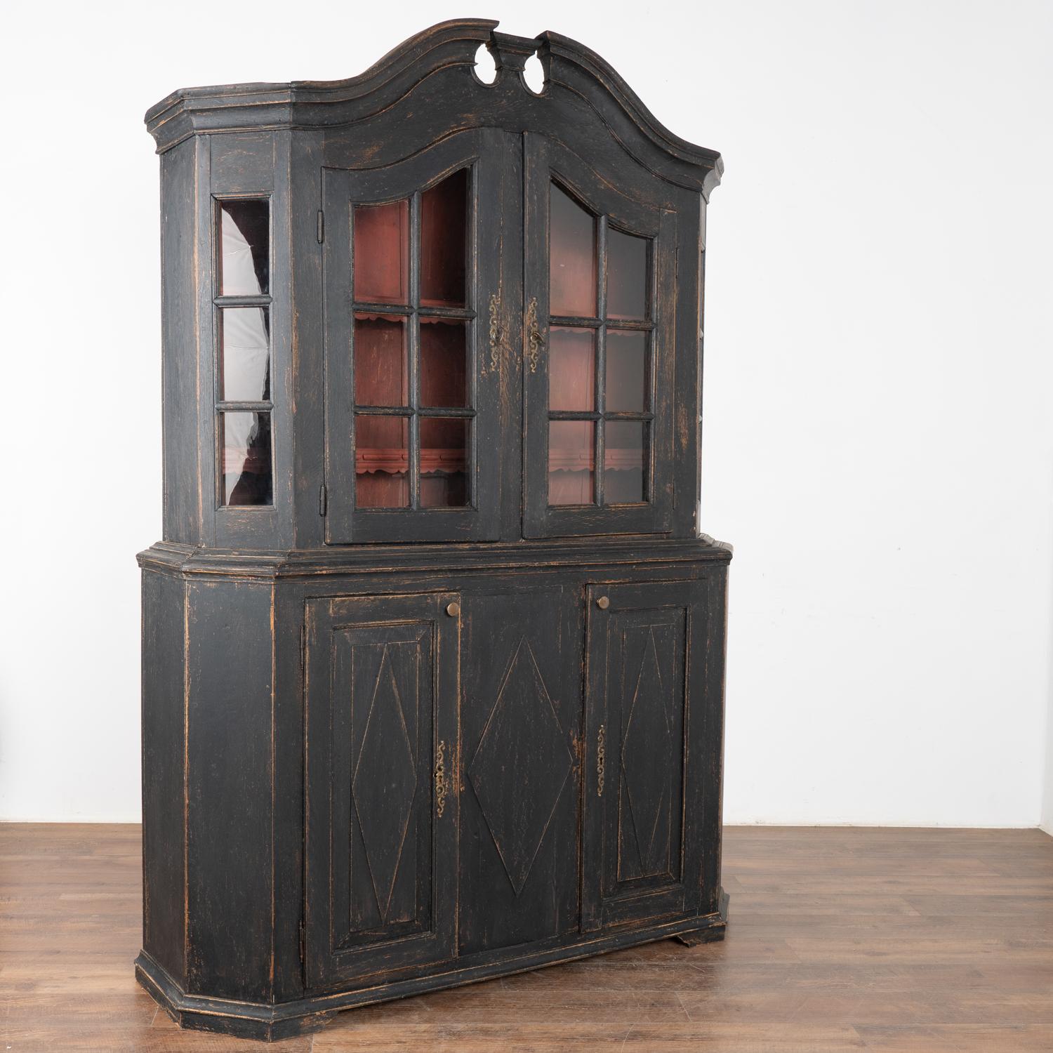 This Danish country pine cupboard may be used as a display cabinet or bookcase. The upper pane glass doors allow for lovely display of any collection held within.
The newer professionally applied black painted finish is lightly distressed to fit the
