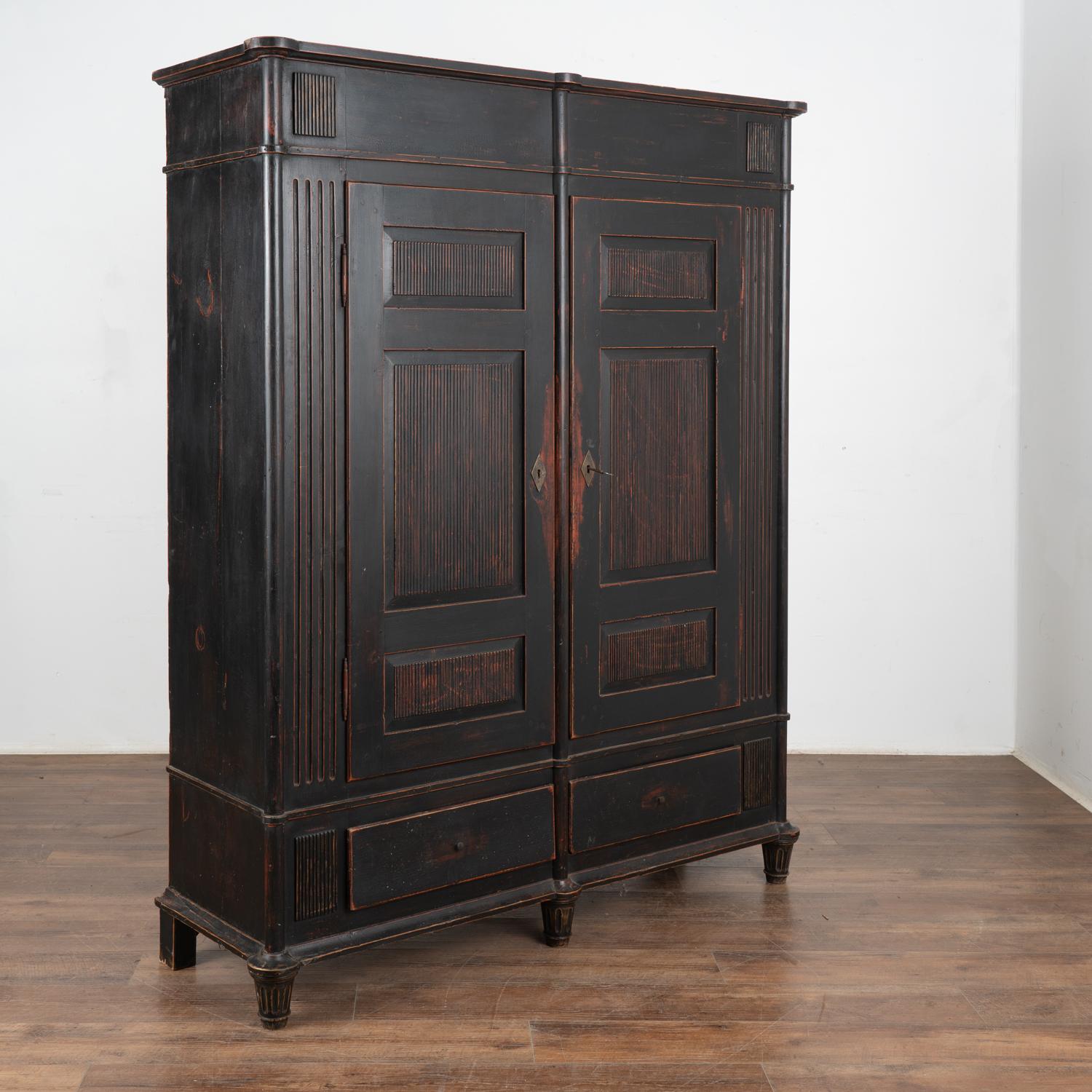This 6' tall pine armoire has been given new life with a recent black painted finish. The finish is lightly distressed to accent the details of the fluted carving along doors and sides, adding dimension and character.
There are two lower drawers and