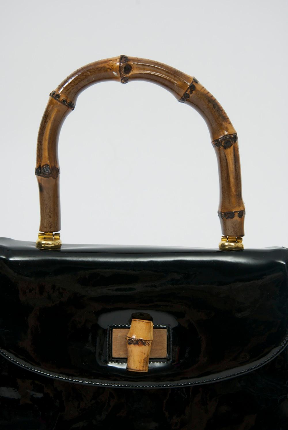 1960s black patent handbag with bamboo handle and clasp is a contemporary replica of a popular Gucci style from the mid twentieth century. Very well made, the red interior is divided into two with two zippered compartments - one in the center and