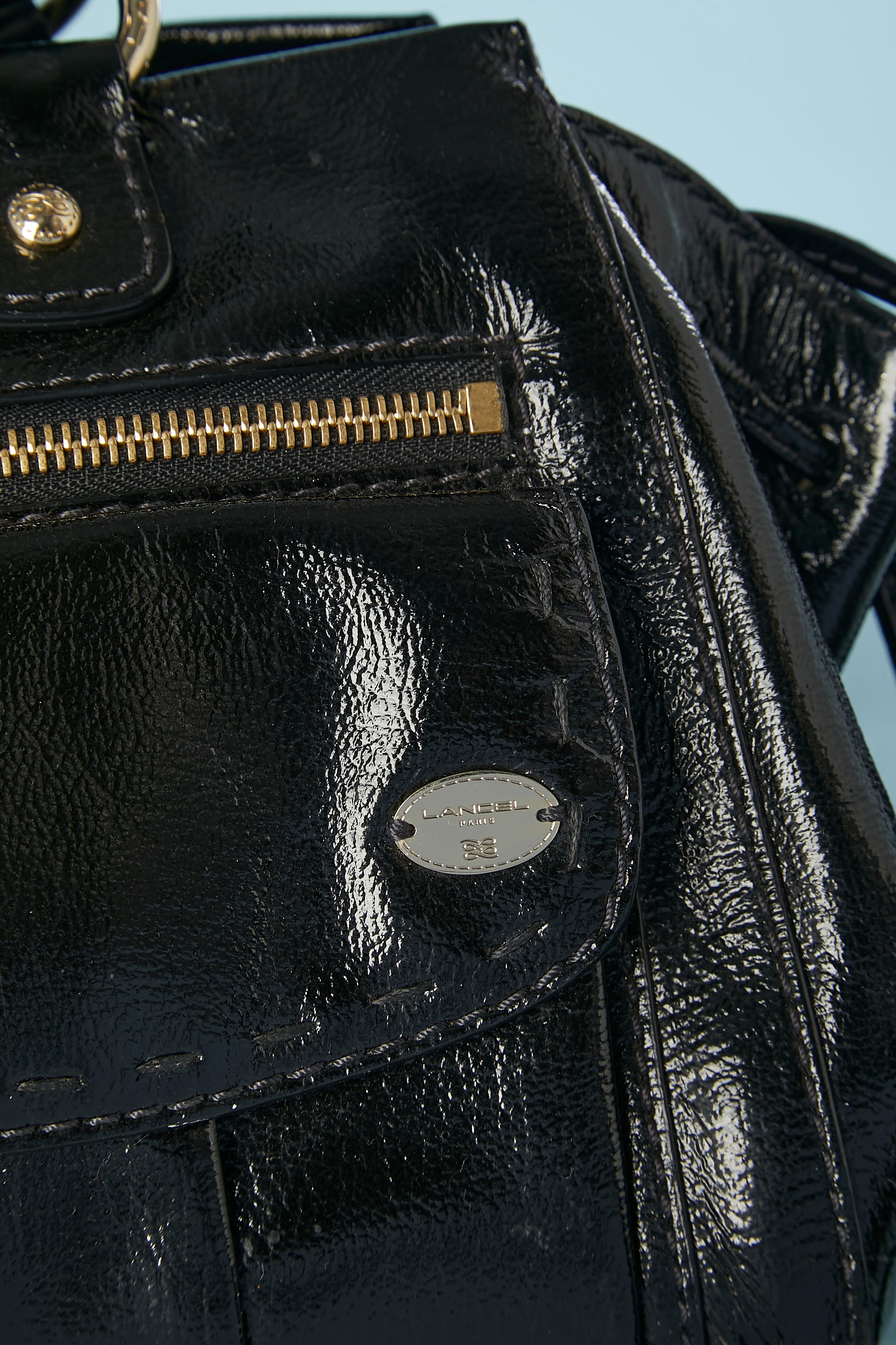 Black patent leather hand-bag. Cotton Toile de Jouy lining. 2 front pockets with magnet snap button and a third one with zip closure. Drawstring on both side ended with pompoms. Slap on the top with magnet snap and zip closure. Mini-purse attached.