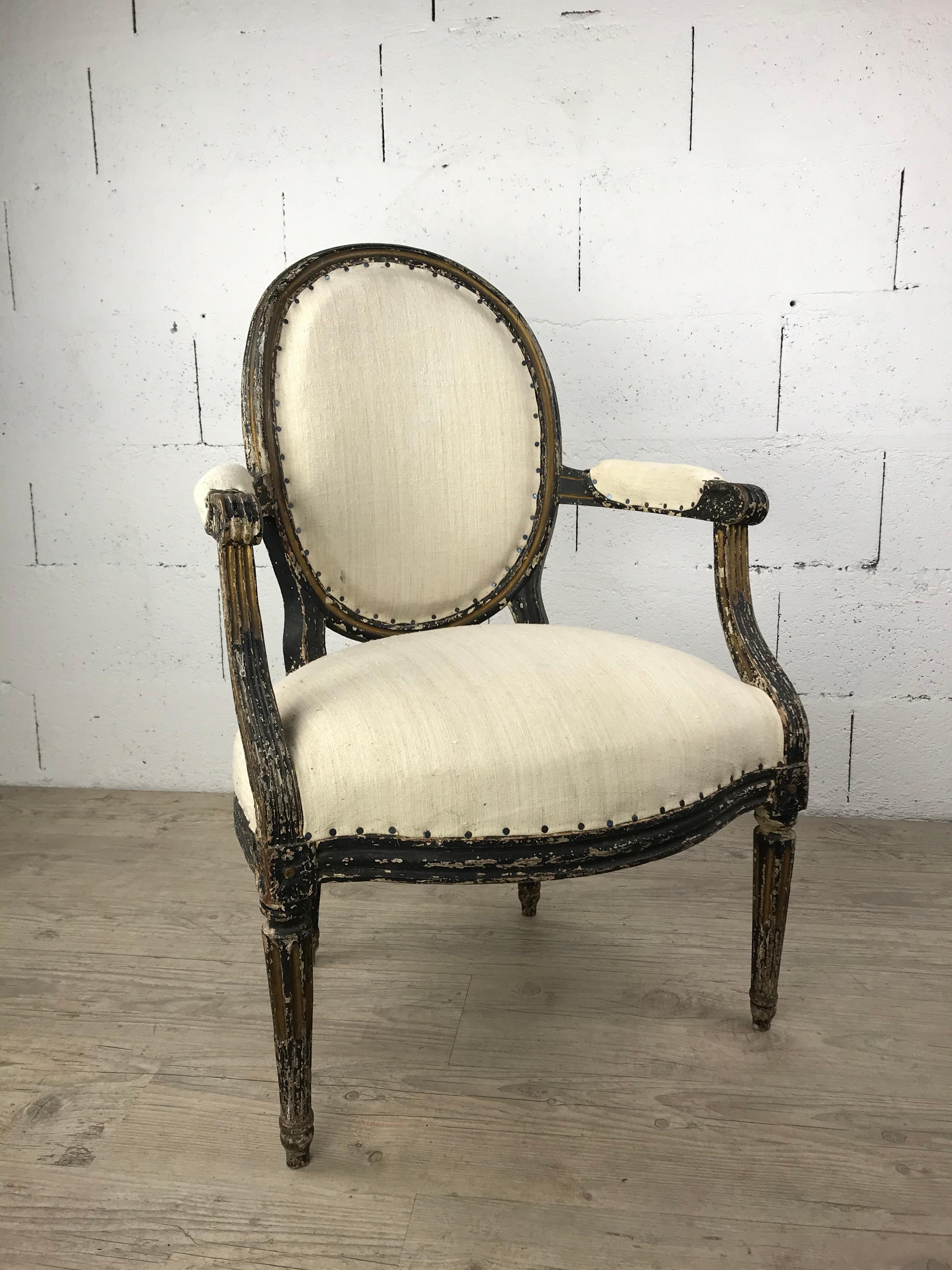 Elegant French armchair in carved and painted wood, dating from the late 18th century. This refined seat embodies the Louis XVI style, with its oval medallion back, straight armrests ending in scrolls, and fluted tapering legs. The frame retains